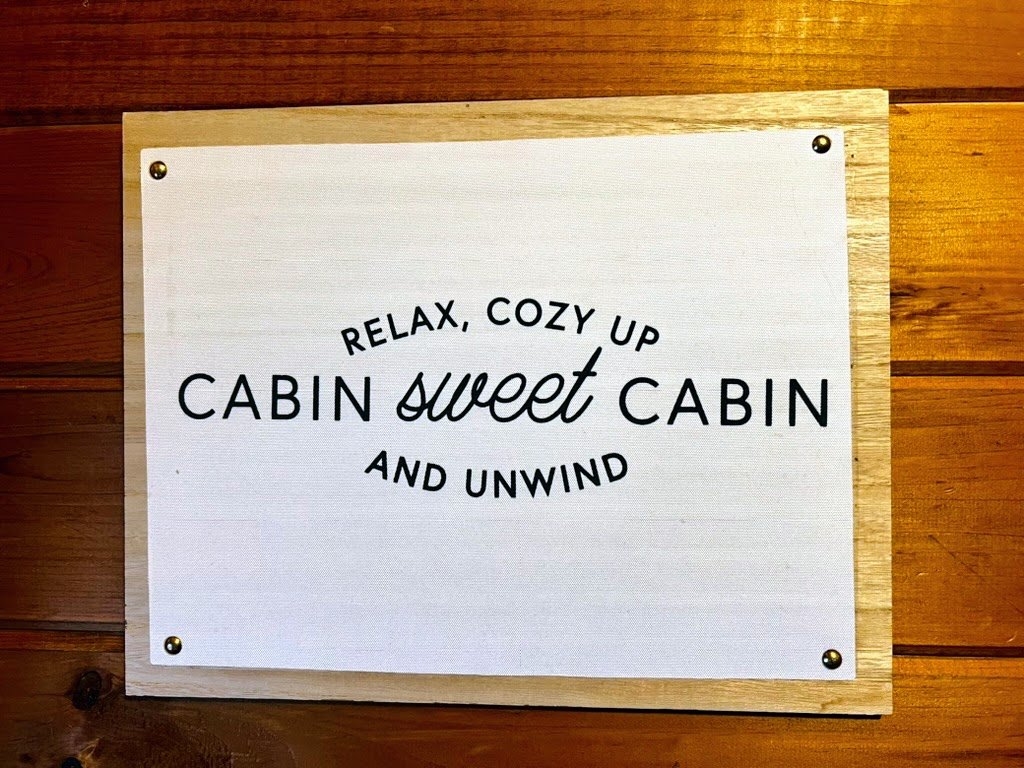 Sign with text "Relax, cozy up, cabin sweet cabin, and unwind" on wooden wall.