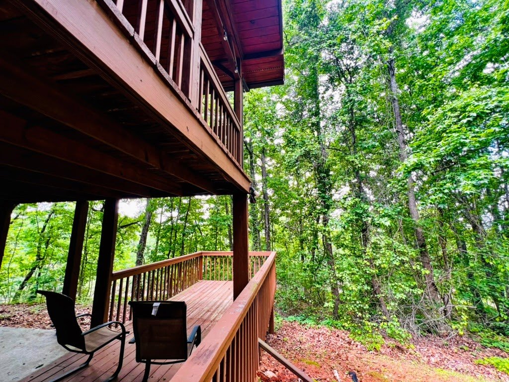 Wooden deck and chairs overlooking a lush, green forest.