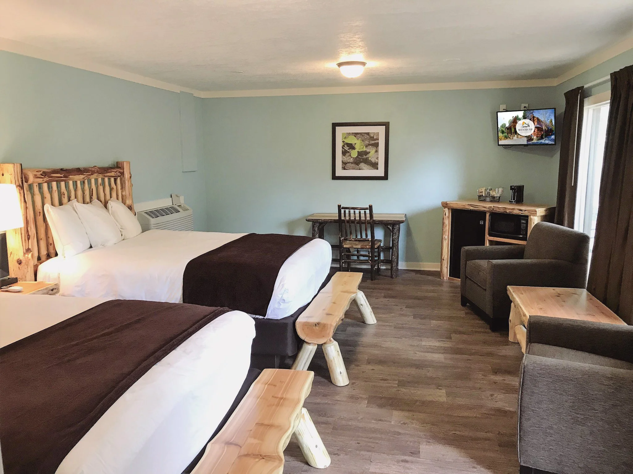 Hotel room with two beds, rustic wooden furniture, small table, chairs, TV, microwave, and armchair.