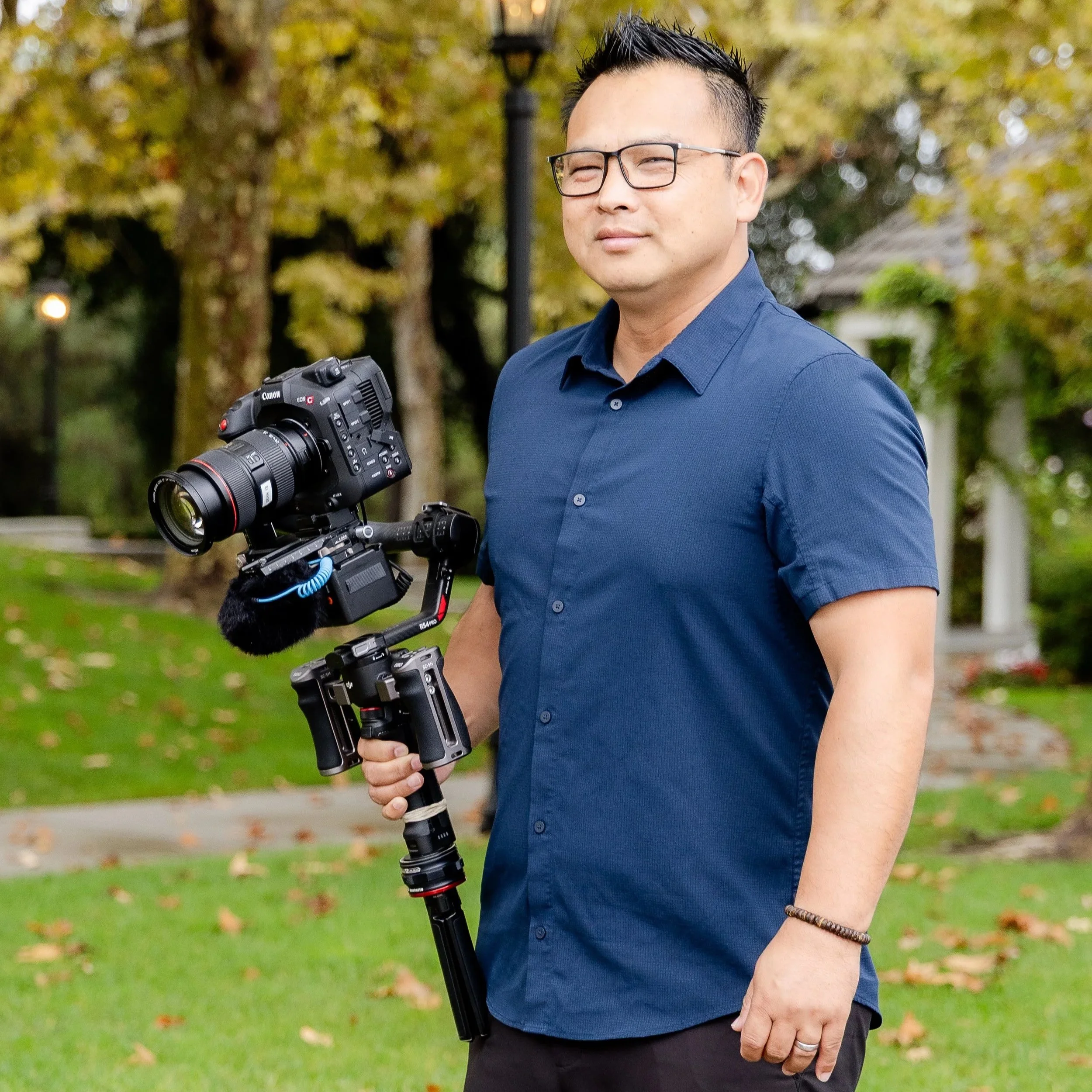 Man smiling, wearing a black collared shirt, short hairstyle, neutral background.