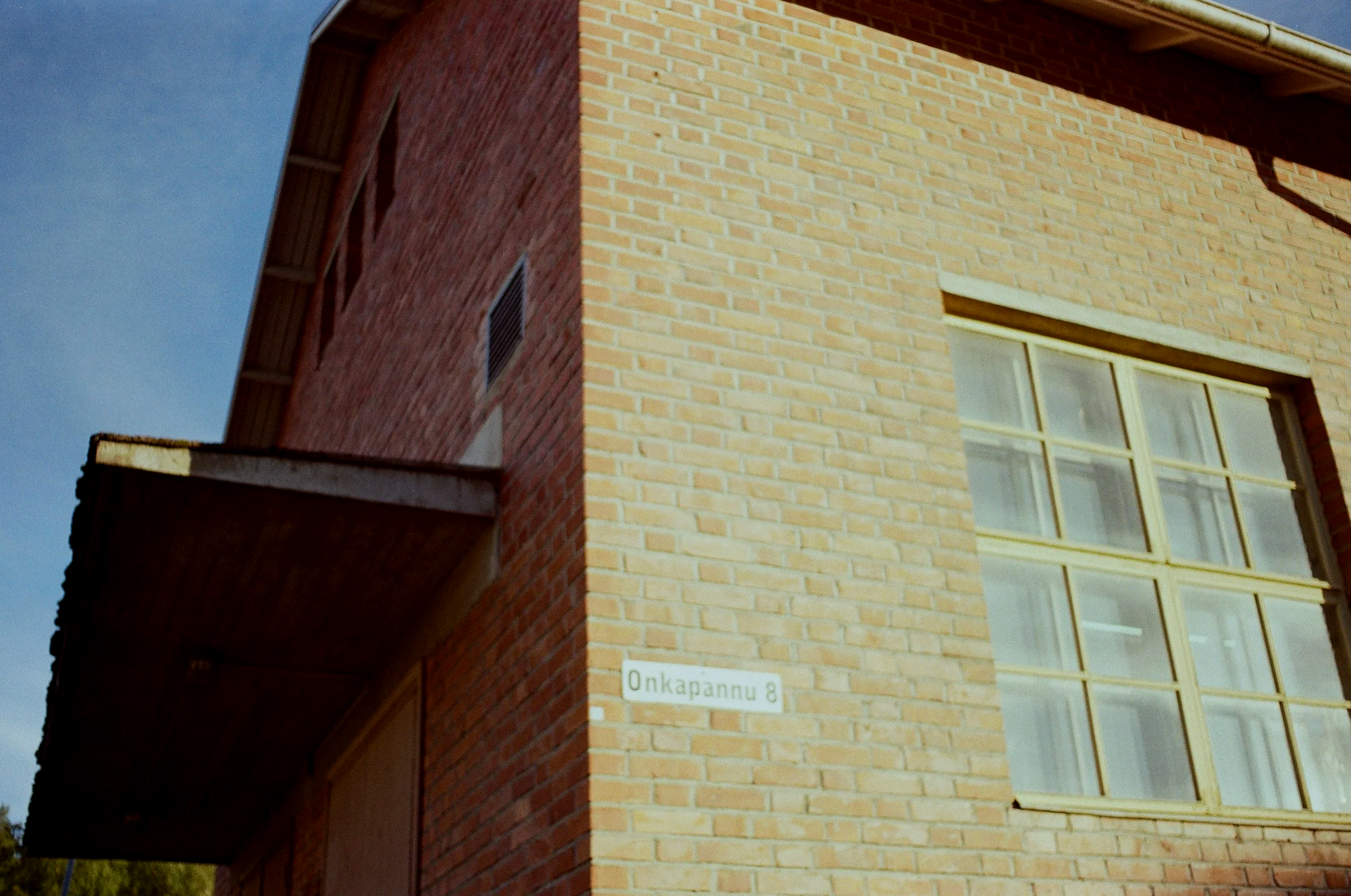 Kuvassa on punainen tiilirakennus, jossa on suuri ikkuna ja katuviittaa 'Onkapanne 8'.