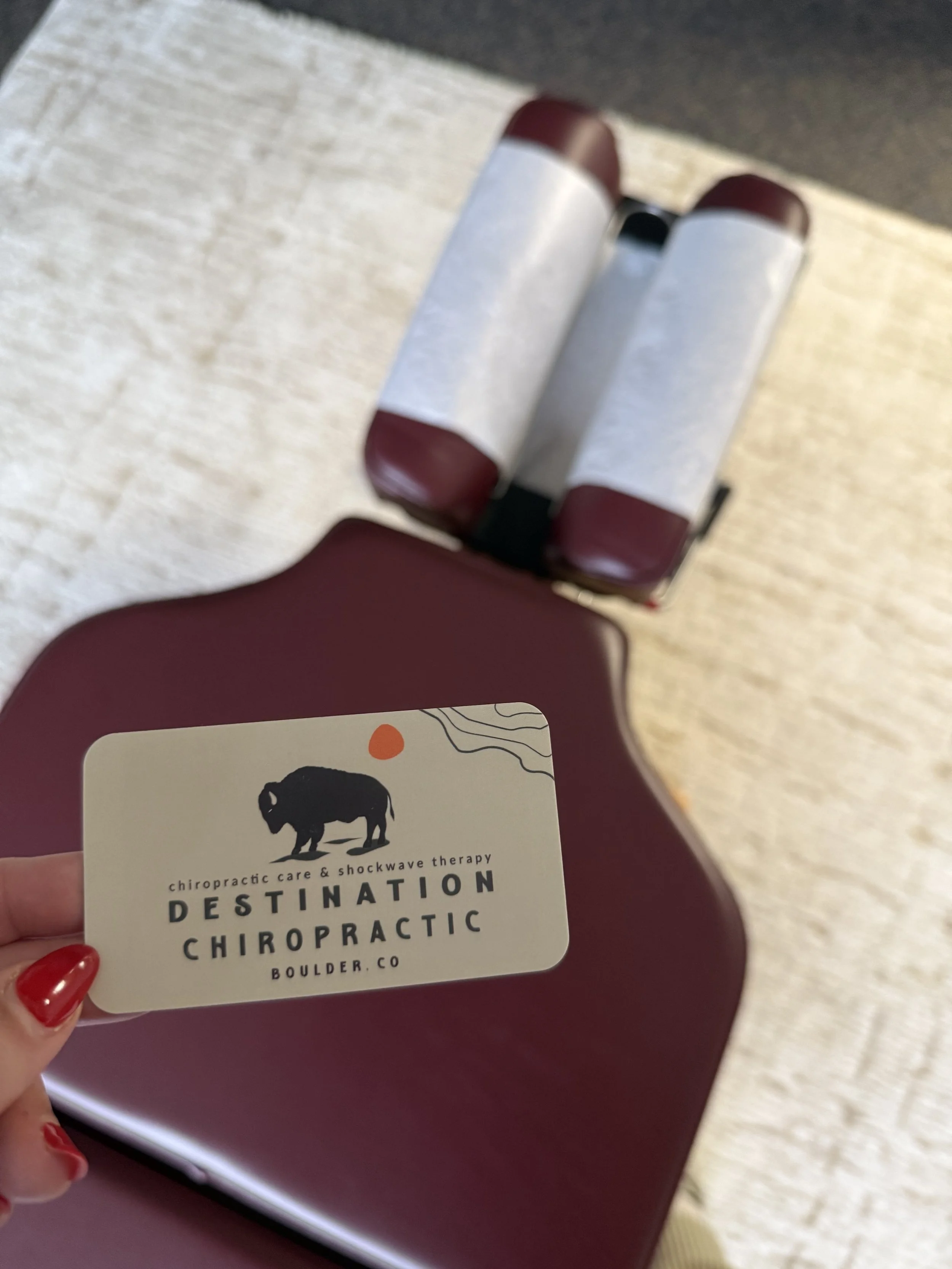 Hand holding a Destination Chiropractic business card over an adjusting table.