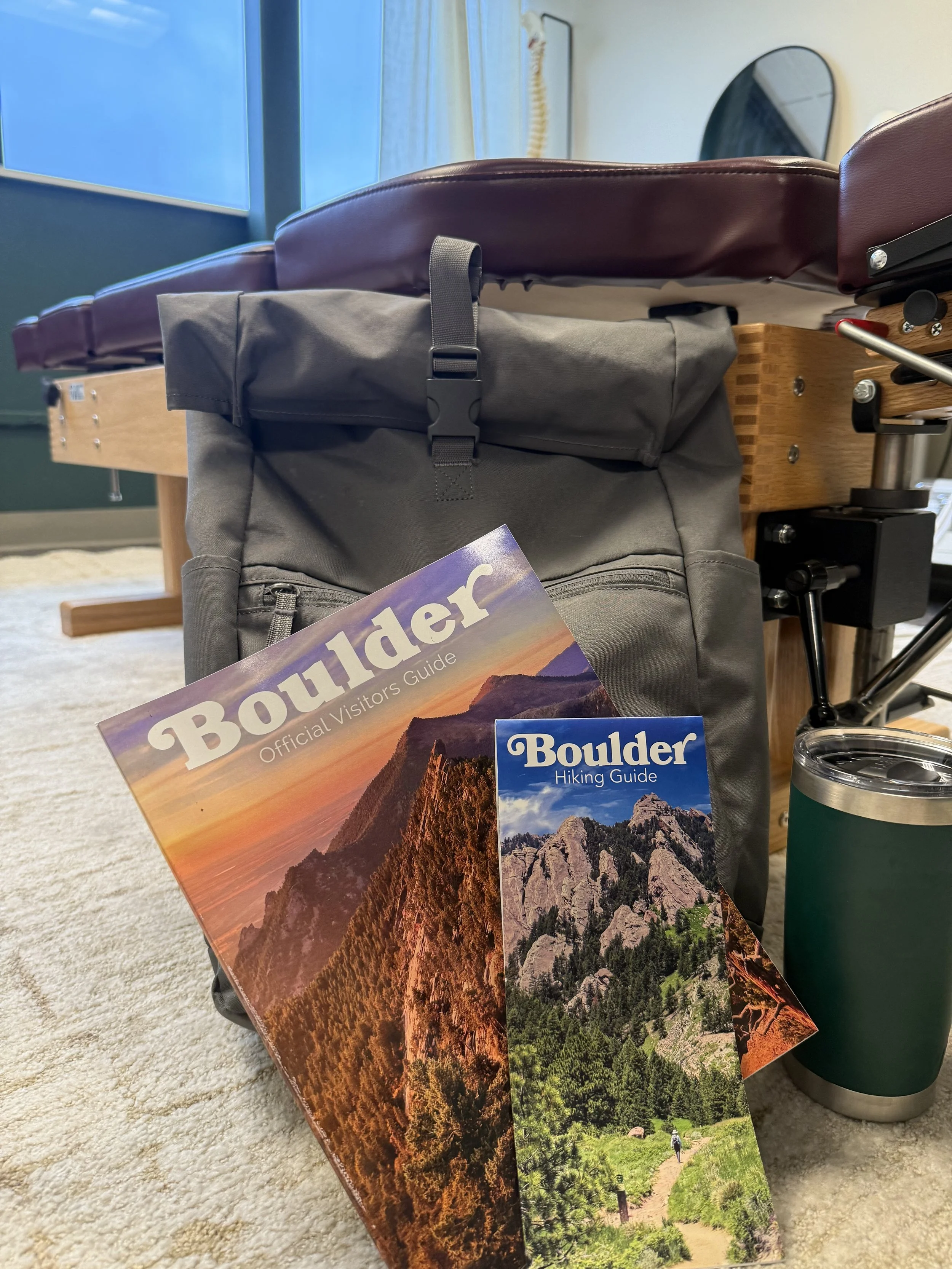 Backpack and Boulder visitor guides beside a chiropractic table for traveler care in Boulder
