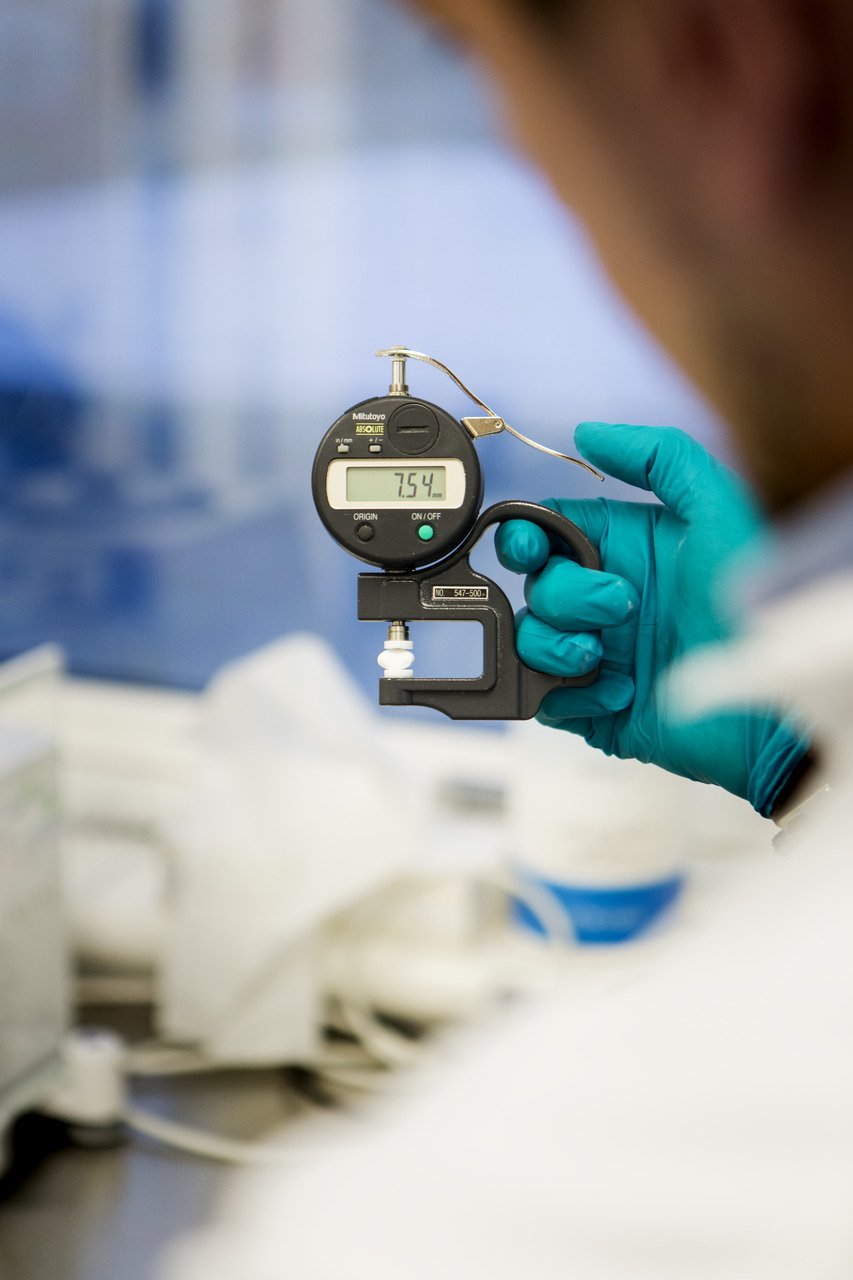 A person wearing blue gloves holding a digital micrometer measuring 7.54.