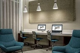 Modern office space with two computers on a desk, swivel chairs, and blue lounge chairs.