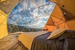Geodesic dome interior with bed, large windows, and view of sky and landscape.