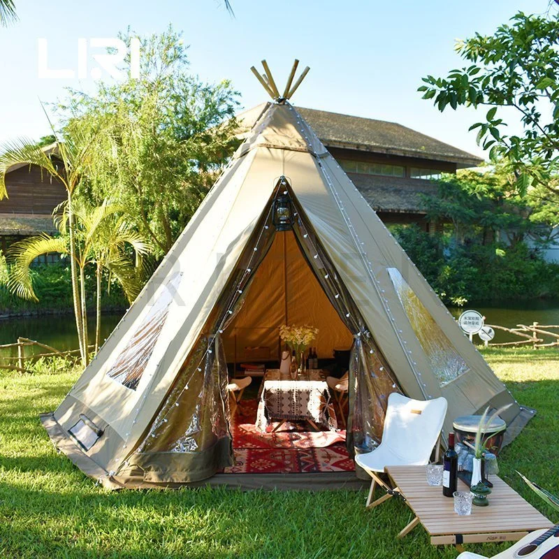 Glamping tent with luxurious interior and outdoor seating on grassy area with trees and a wooden building in the background.