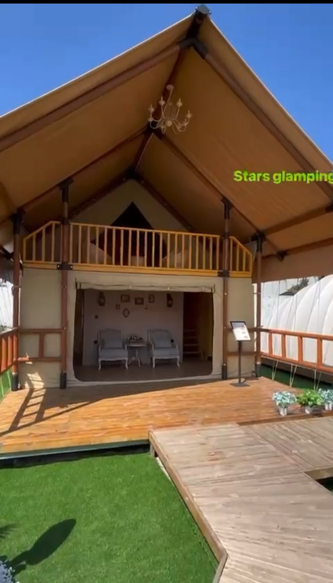 A wooden house with a steep roof, chandelier, and balcony, with an outdoor patio with chairs and potted plants.
