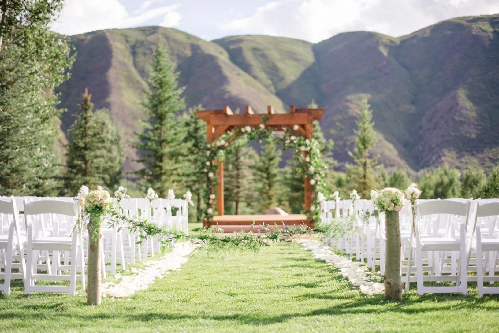 Outdoor wedding ceremony setup with white chairs and floral decorations, set against a mountain backdrop.