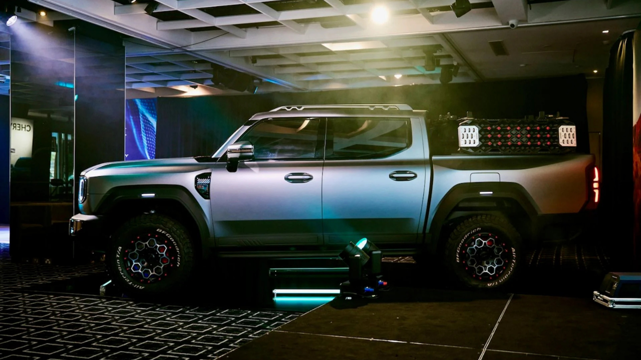 Perfil lateral de pickup eléctrica Chery plateada en escenario con neumáticos todoterreno y rack de carga.