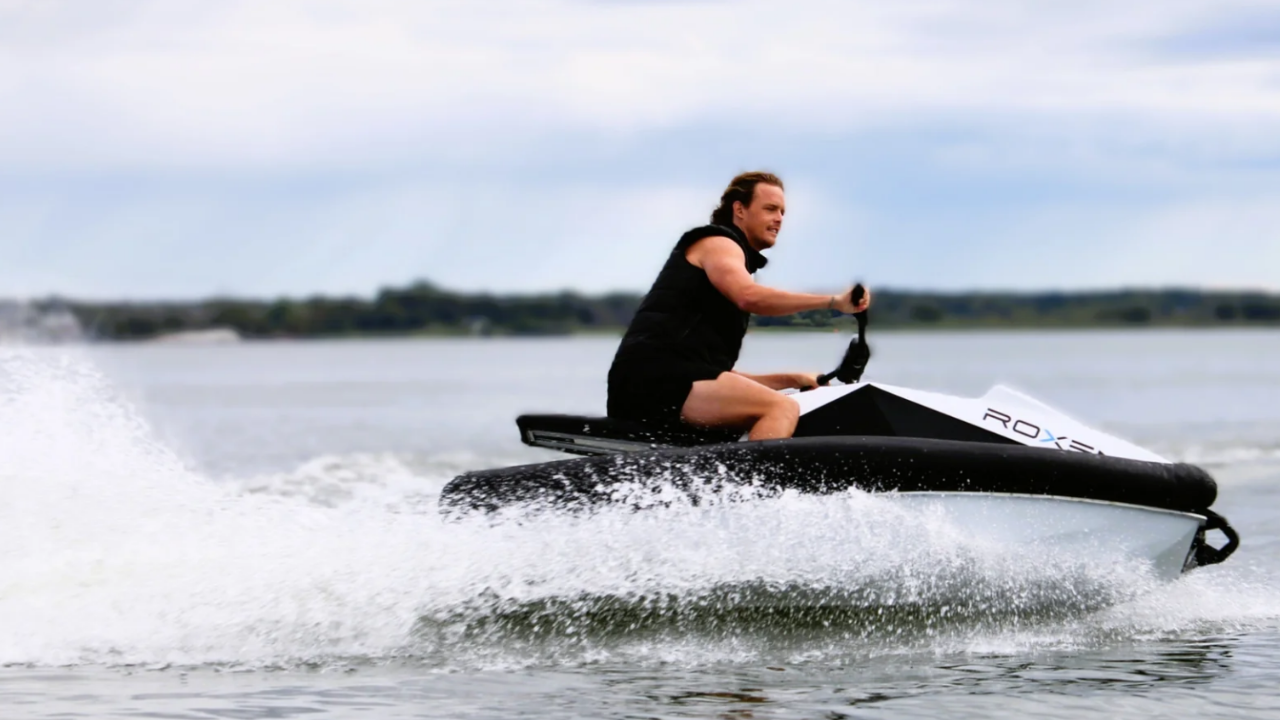 Hombre en moto de agua eléctrica Roxen blanca cruzando el agua con gran estela, mostrando potencia náutica eléctrica.