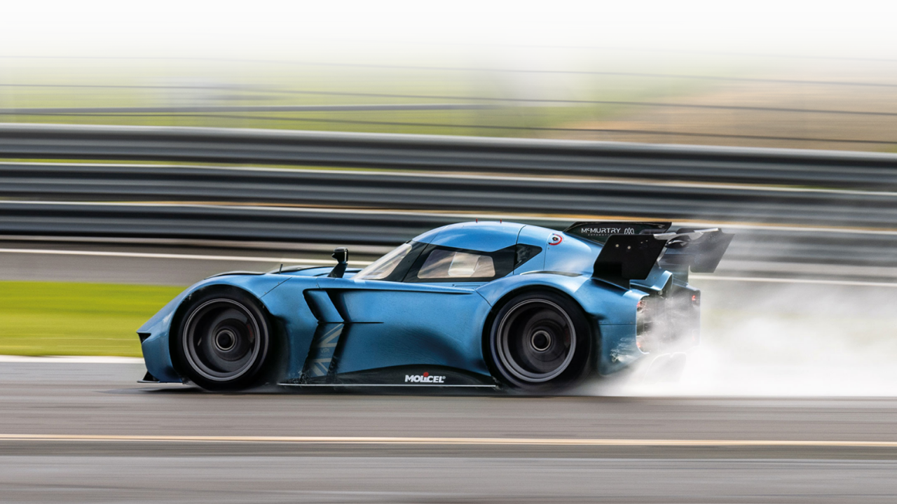 McMurtry Spéirling azul metálico a alta velocidad en pista con estela de succión por ventiladores y desenfoque.
