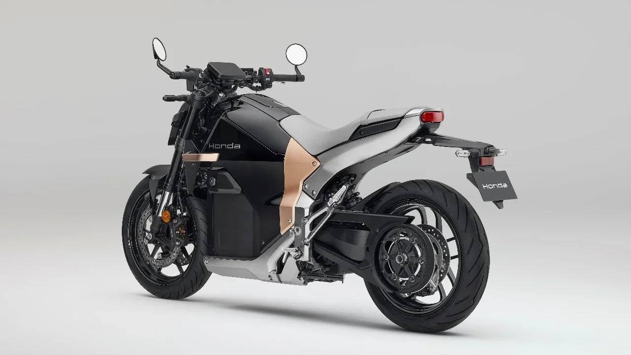 Vista trasera en tres cuartos de un prototipo de moto eléctrica Honda negra y bronce en un estudio blanco.