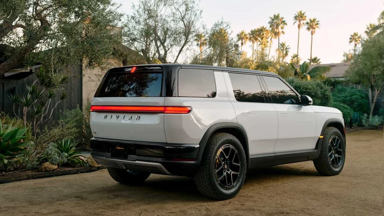 Trasera de Rivian R2 blanco glaciar bajo palmeras en California, destacando su barra de luces LED y diseño moderno.