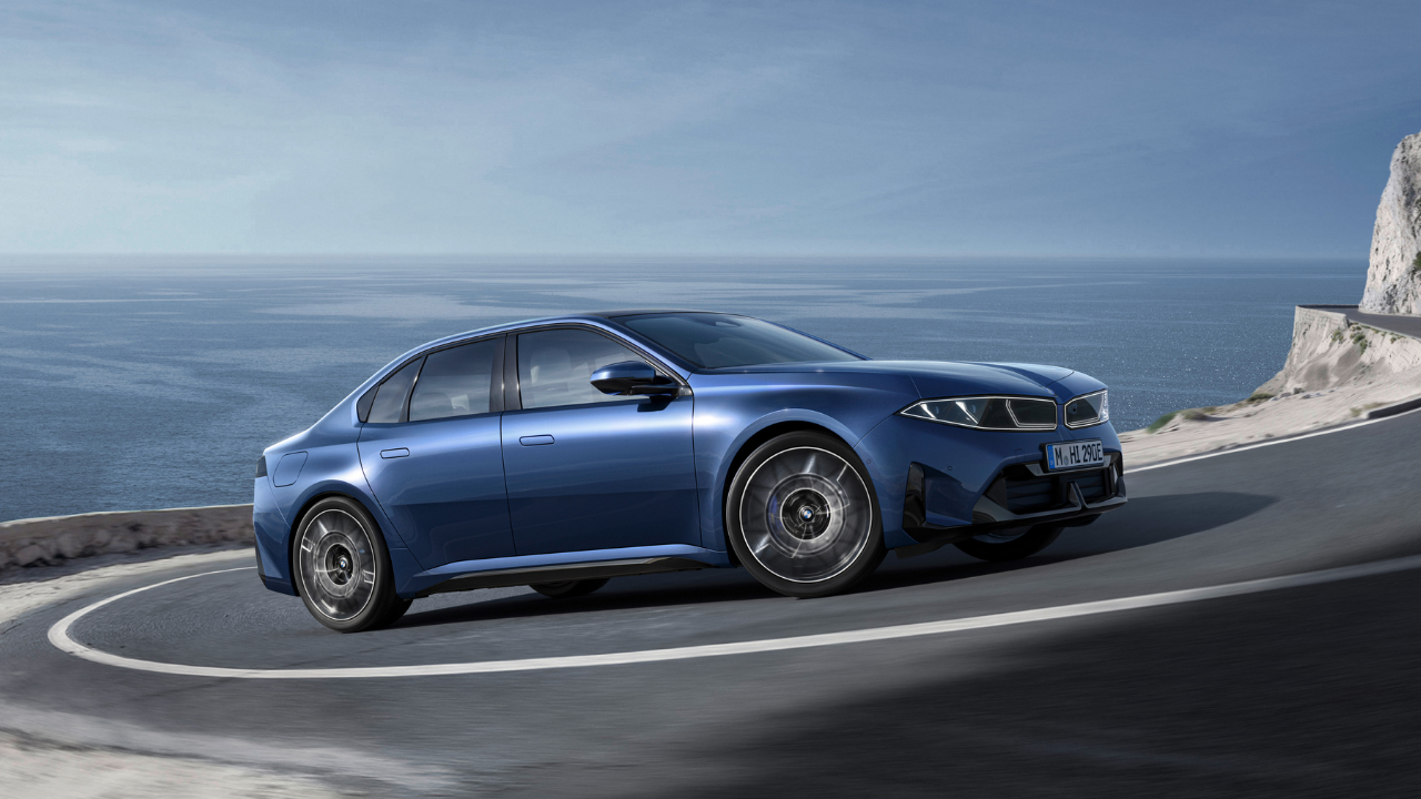 Render de un BMW eléctrico azul tomando una curva en una carretera costera soleada, destacando el rendimiento EV.