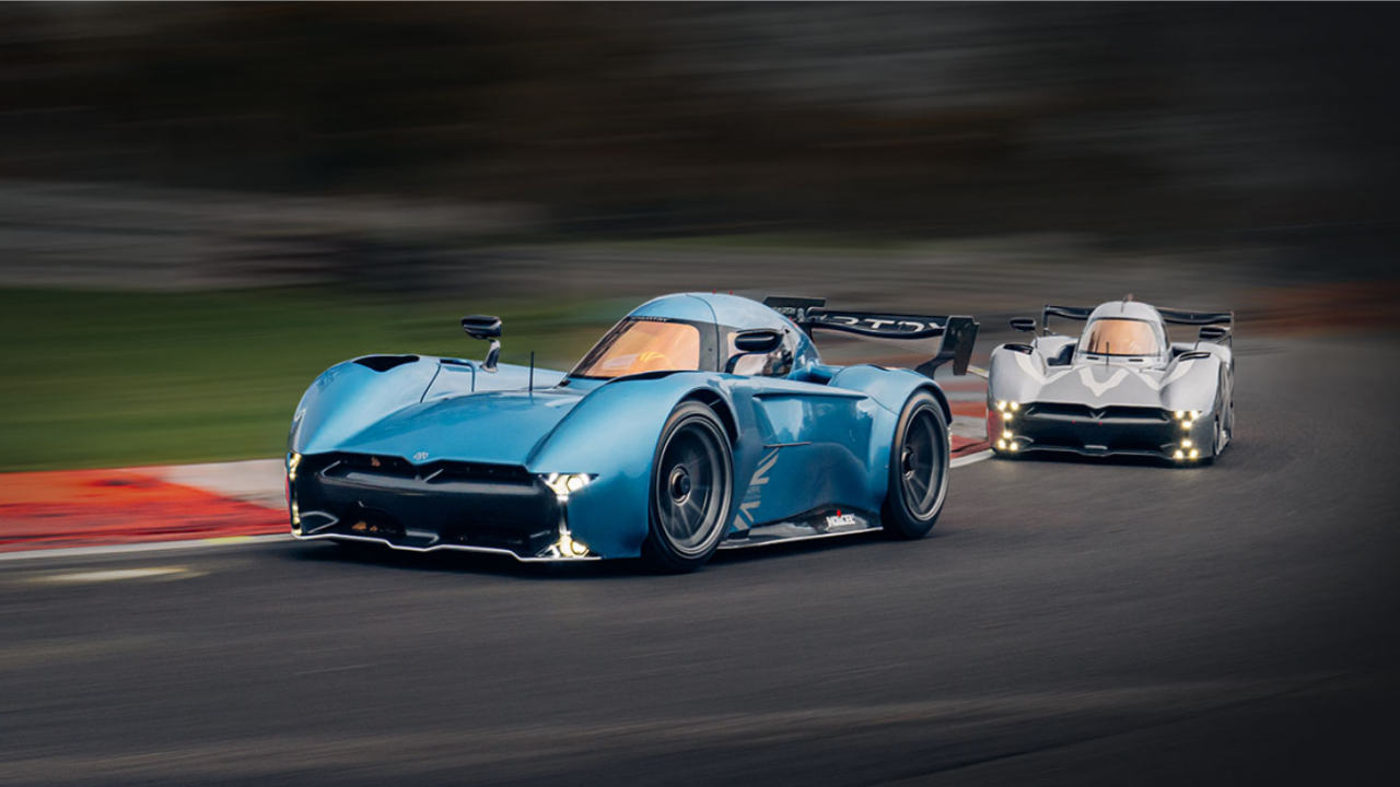 Coches McMurtry Spéirling azul y plata tomando una curva durante una sesión de carreras eléctricas en pista.