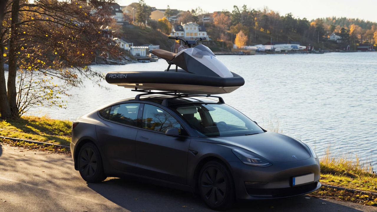 Tesla Model 3 gris mate cargando una moto de agua eléctrica Roxen blanca en el portaequipajes junto a un lago.