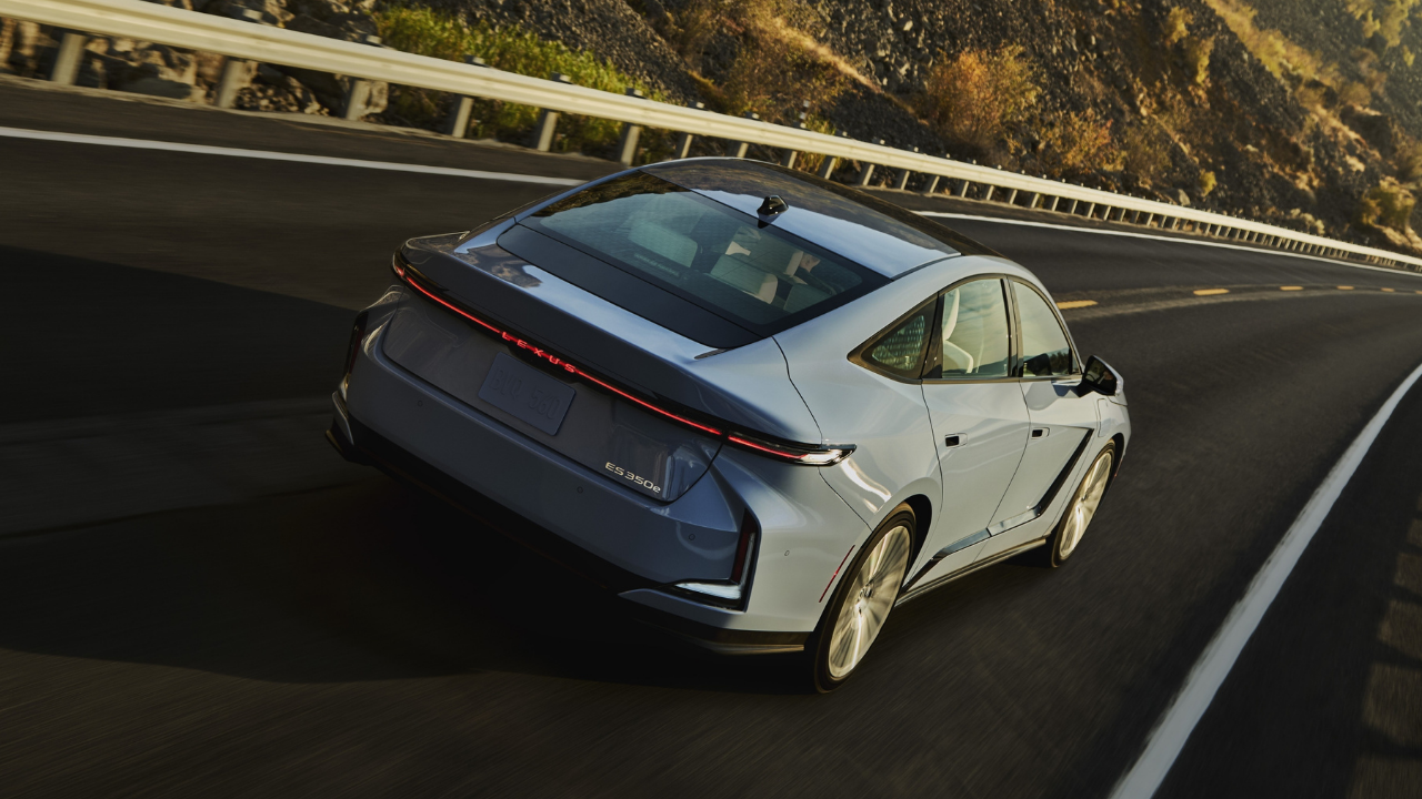 Imagen del Lexus ES 350e azul circulando por una carretera sinuosa al atardecer, destacando su barra de luz trasera.