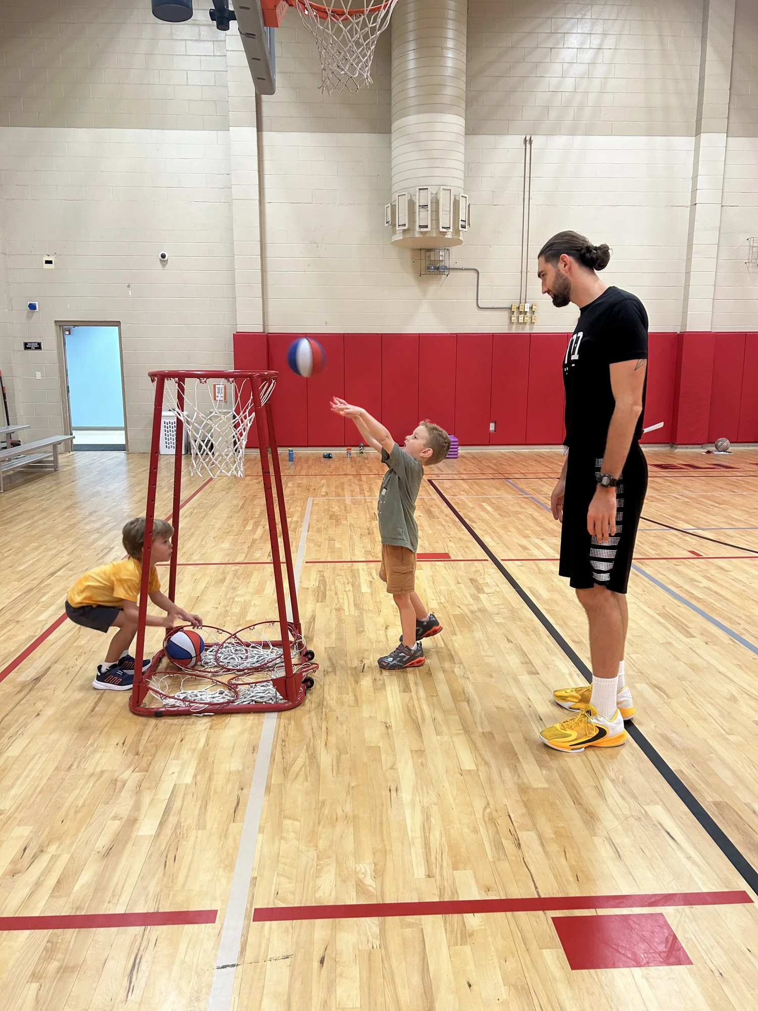 Children shooting hoops with a coach in the Shalom Orlando gym