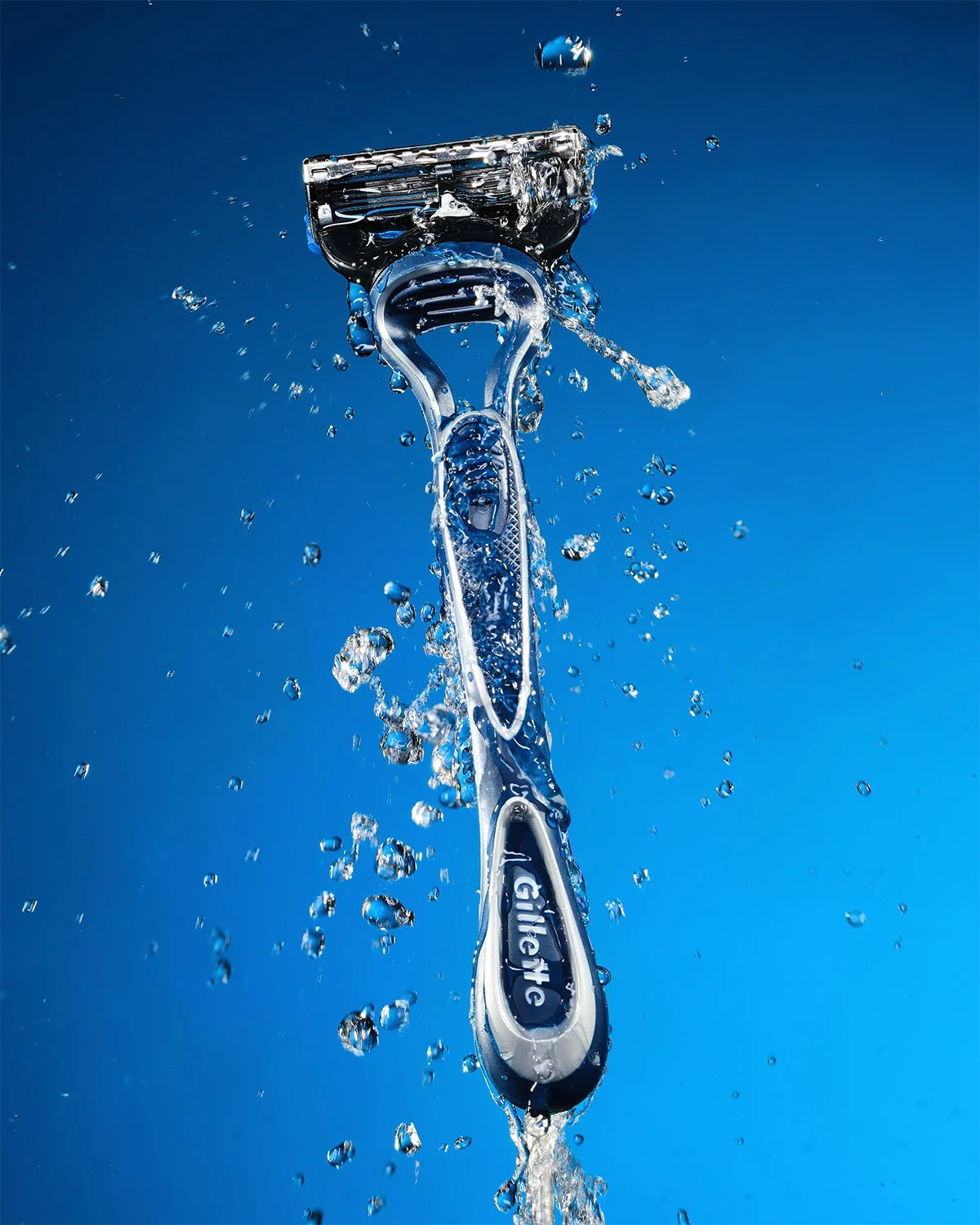 A close-up photo of a razor shaving device with water splashing around it against a blue background.