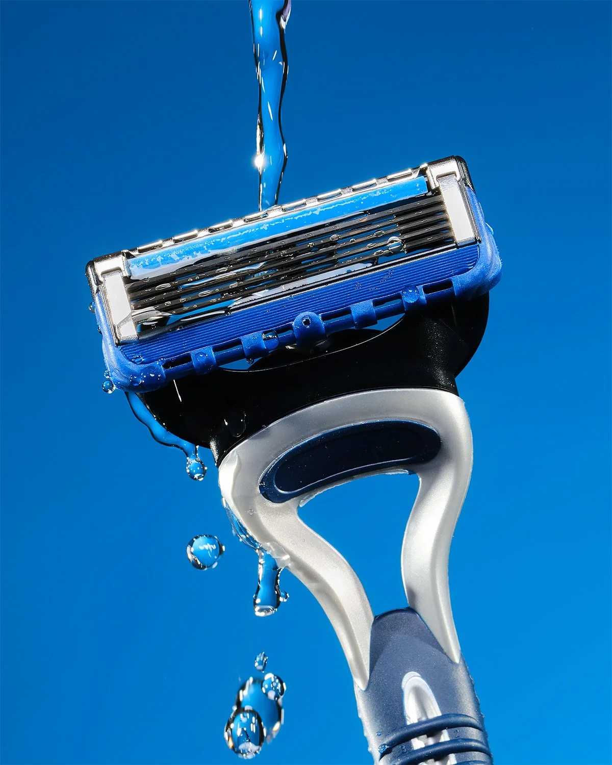 Close-up of a razor with water droplets and flowing water on a blue background.