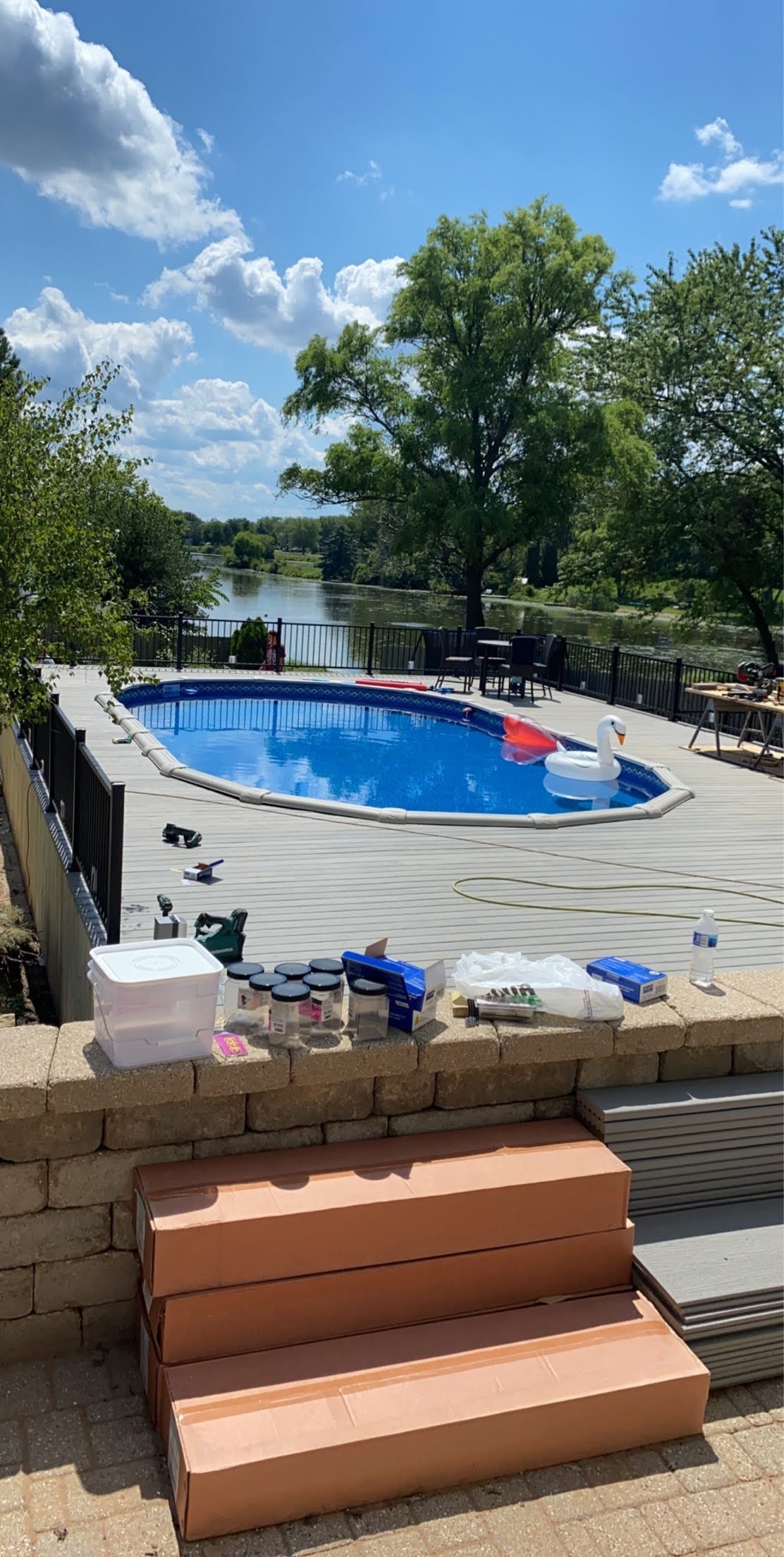A backyard scene with a swimming pool, set on a wooden deck, near a body of water. The pool has a wrap around composite TREX deck. Hidden fastener system.