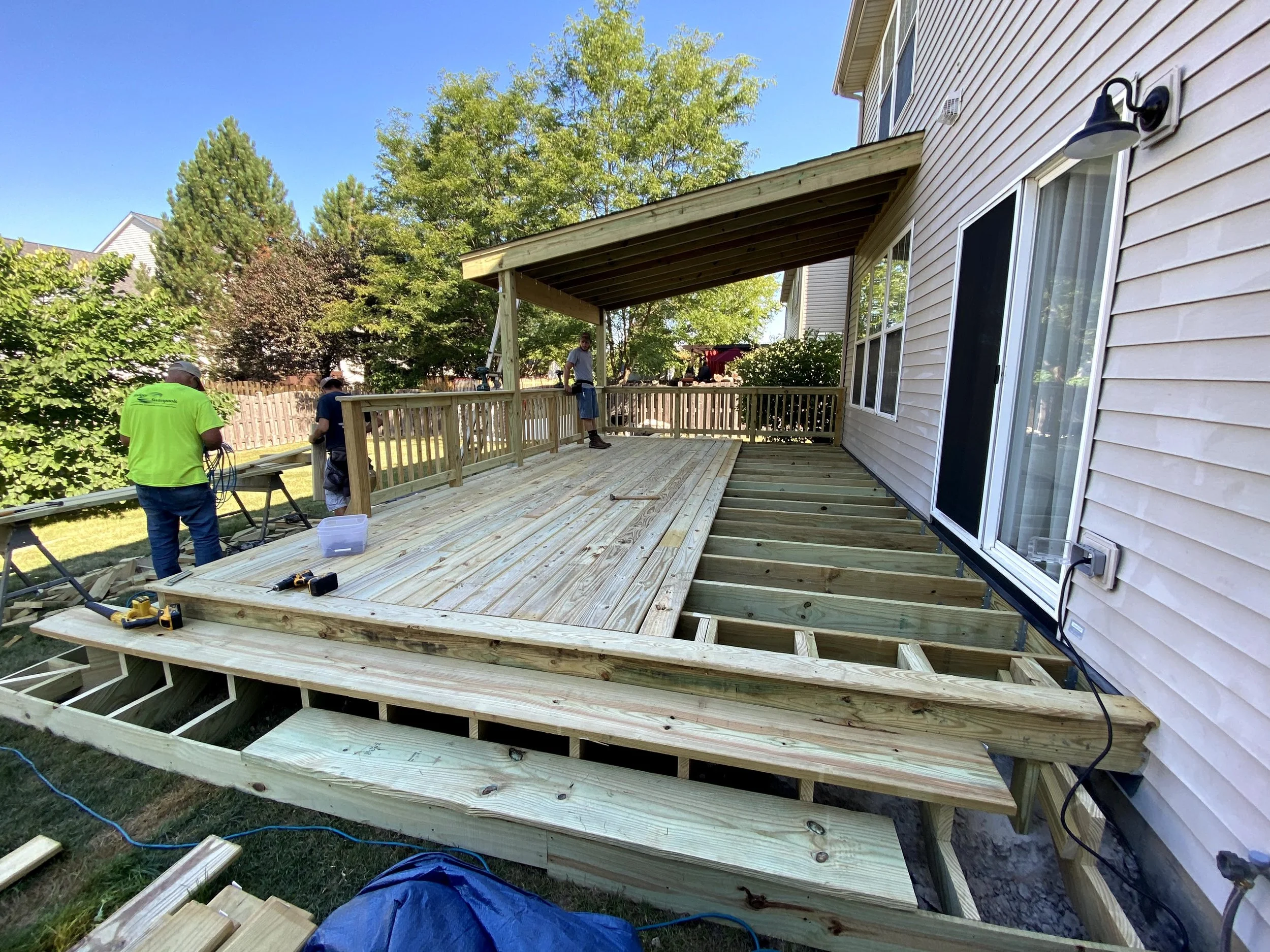People construction workers building a wooden deck outside a house on a sunny day.