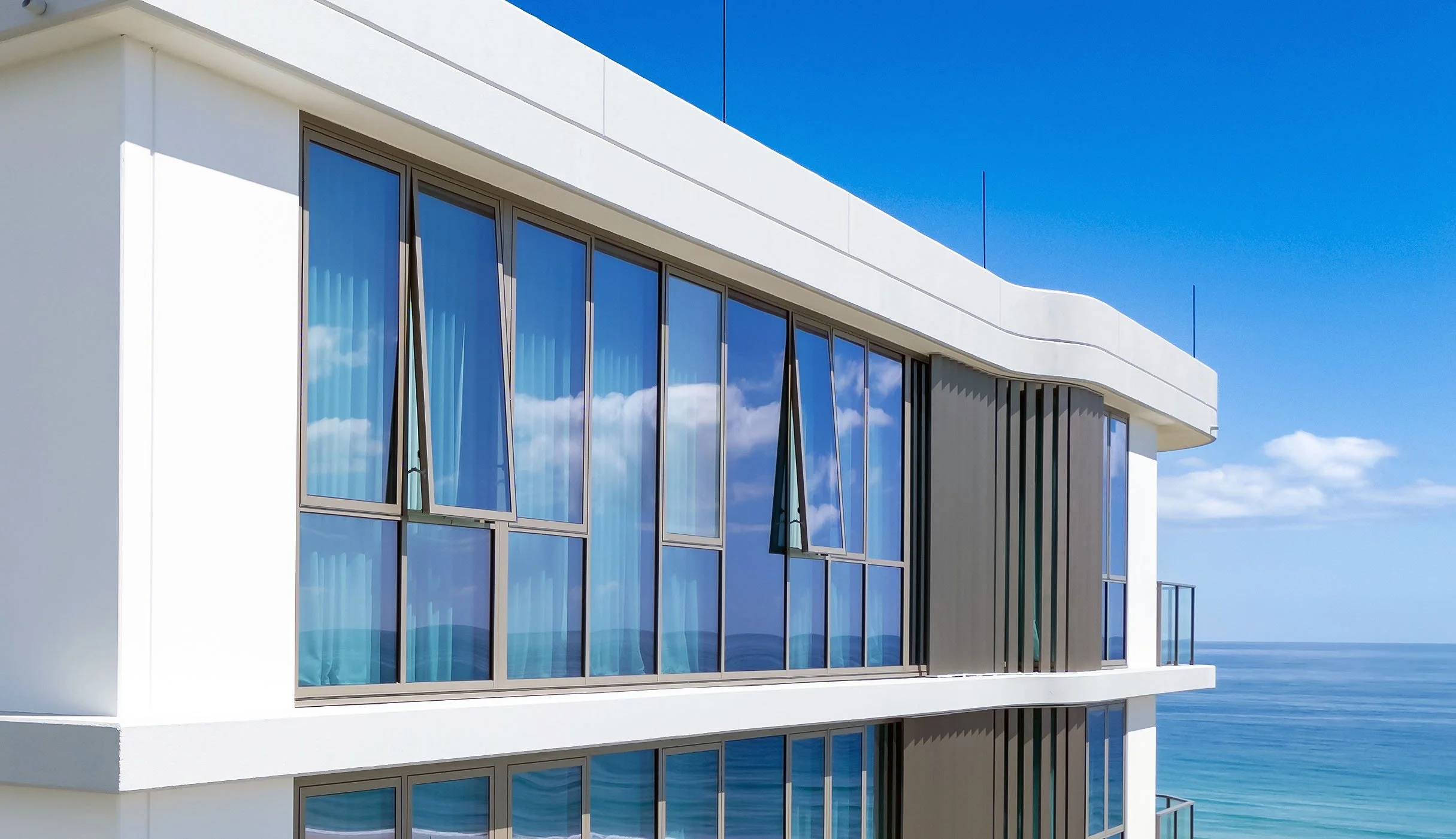 A modern building with large glass windows, overlooking the ocean and blue sky.