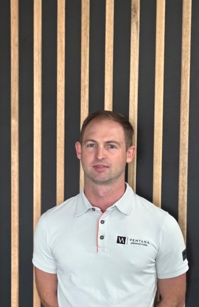A man wearing a white polo shirt standing in front of a wooden slat wall.