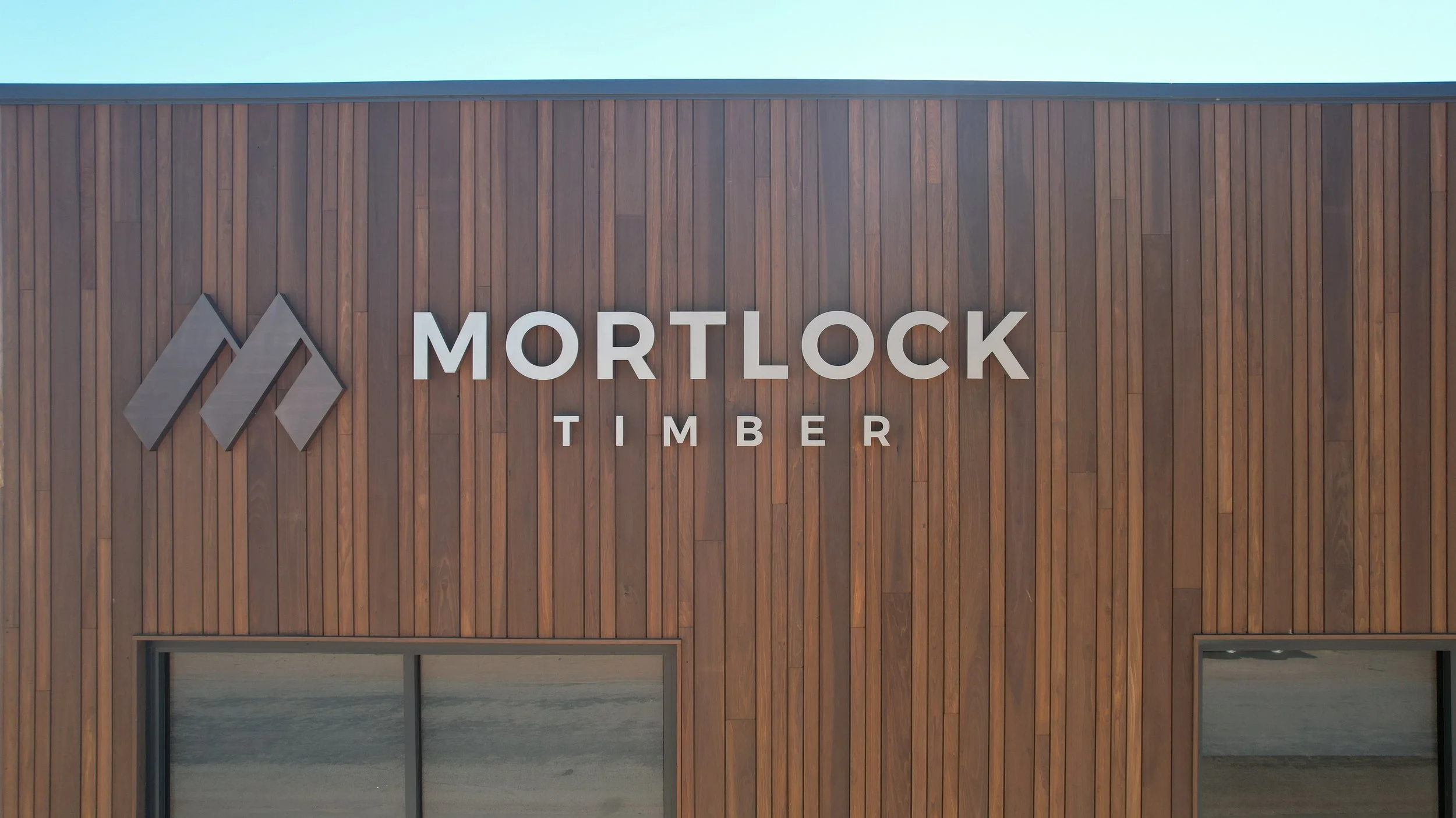 Exterior of a building with wooden paneling and a sign that says 'Mortlock Timber' with a mountain-shaped logo.