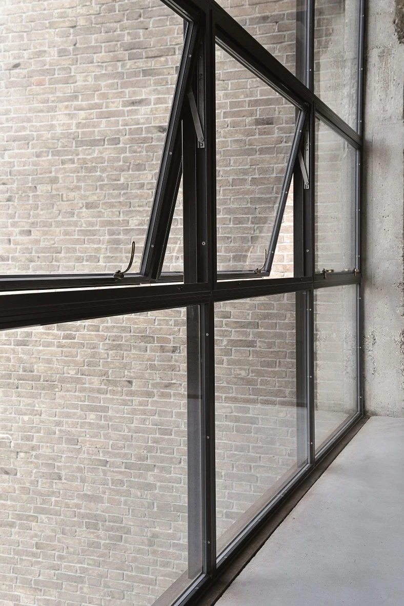Close-up of an open black-framed window with a brick wall in the background.