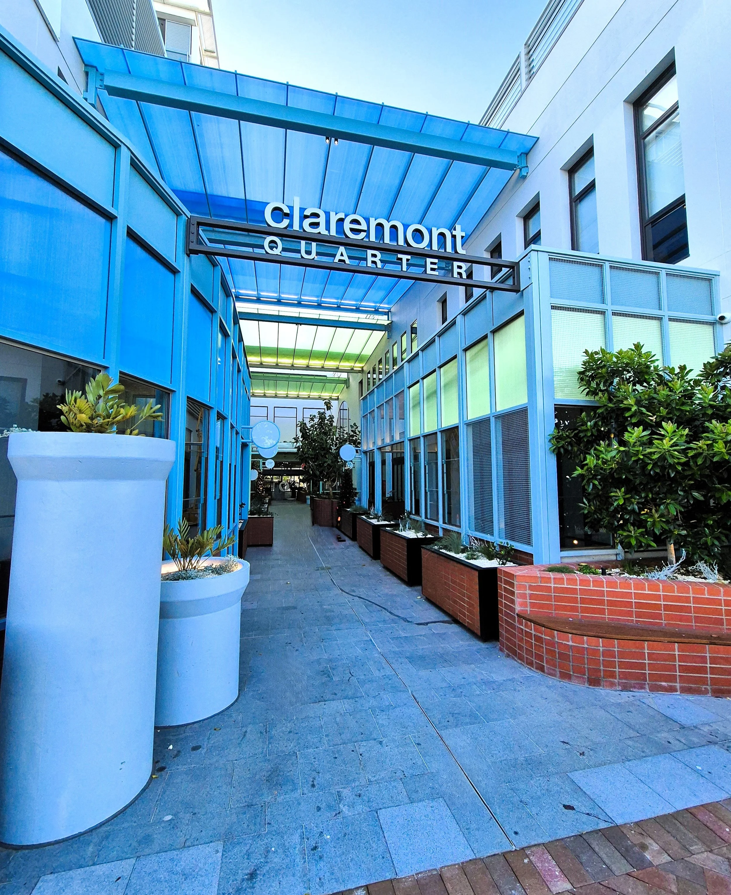 Claremont Quarter shopping area entrance with potted plants and blue structural canopy.