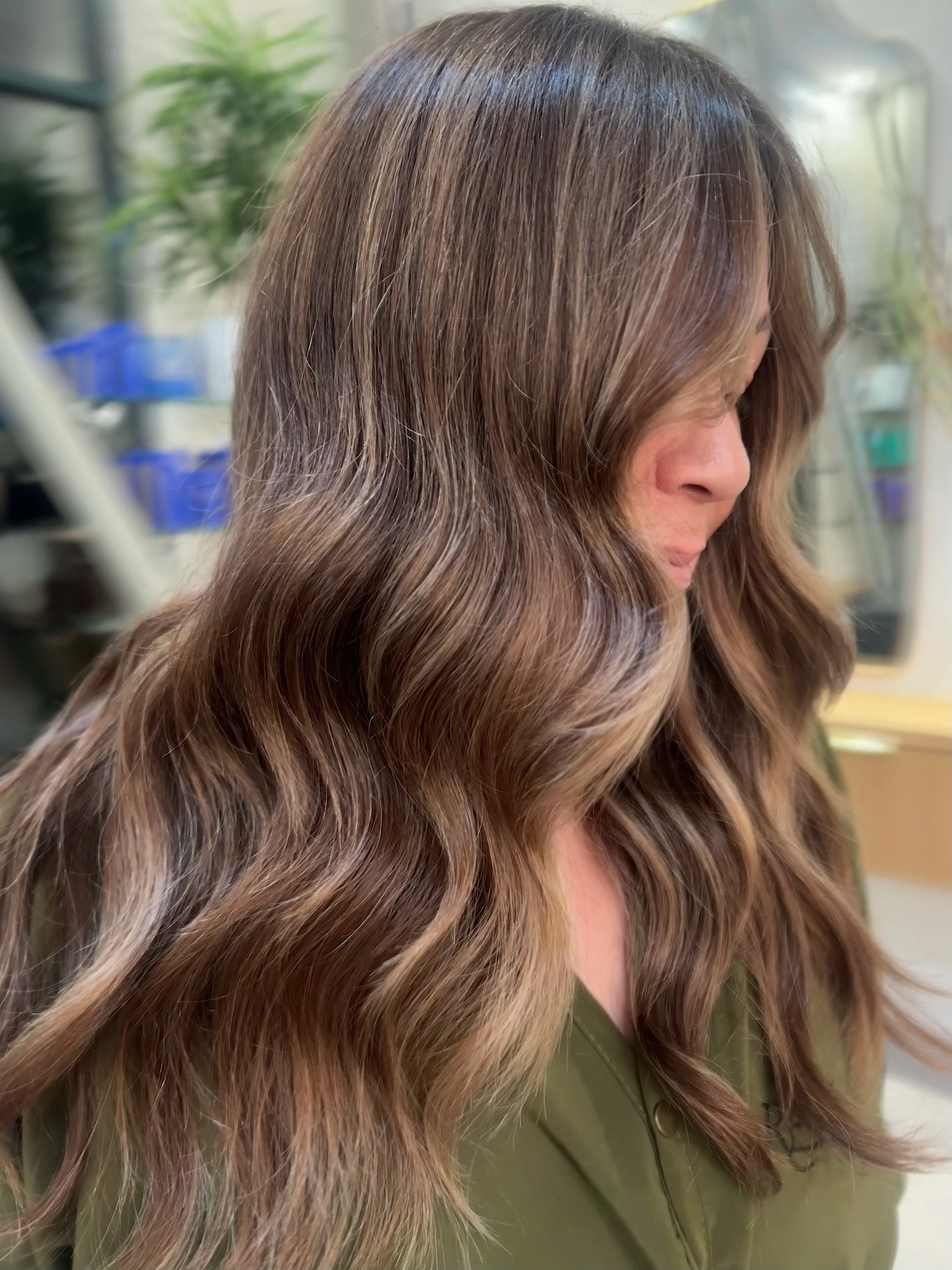 Side profile of a woman with long, wavy, light brown hair wearing an olive green jacket.