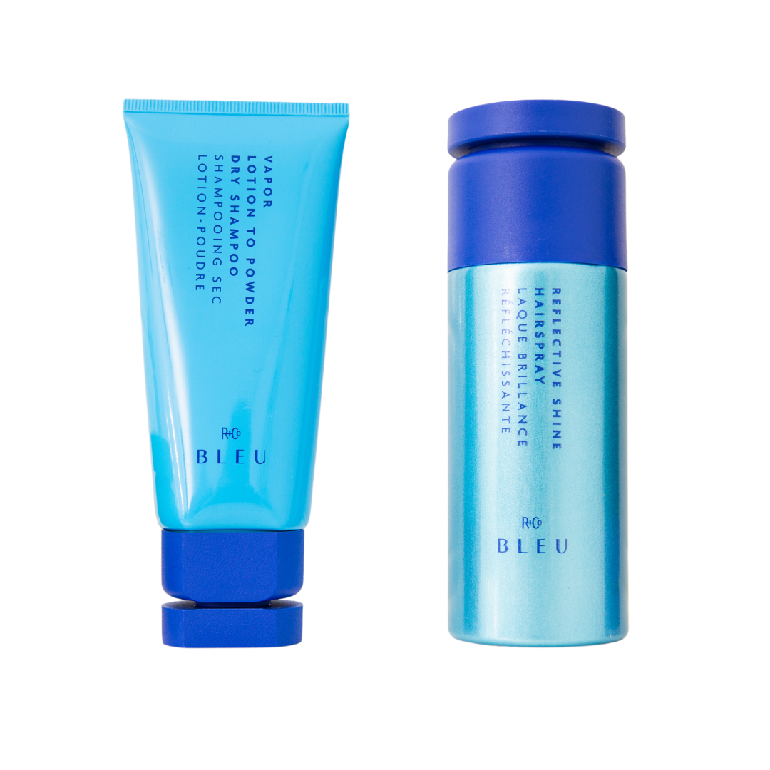 Two skincare products from R+Co BLEU line, featuring a bright blue tube with a blue cap and a cylindrical blue bottle with a blue cap. The tube is labeled as 'Vapor Lotion to Powder Dry Shampoo Sec' and the bottle is labeled 'Reflective Shine Hairpray with Laque Brillance.'
