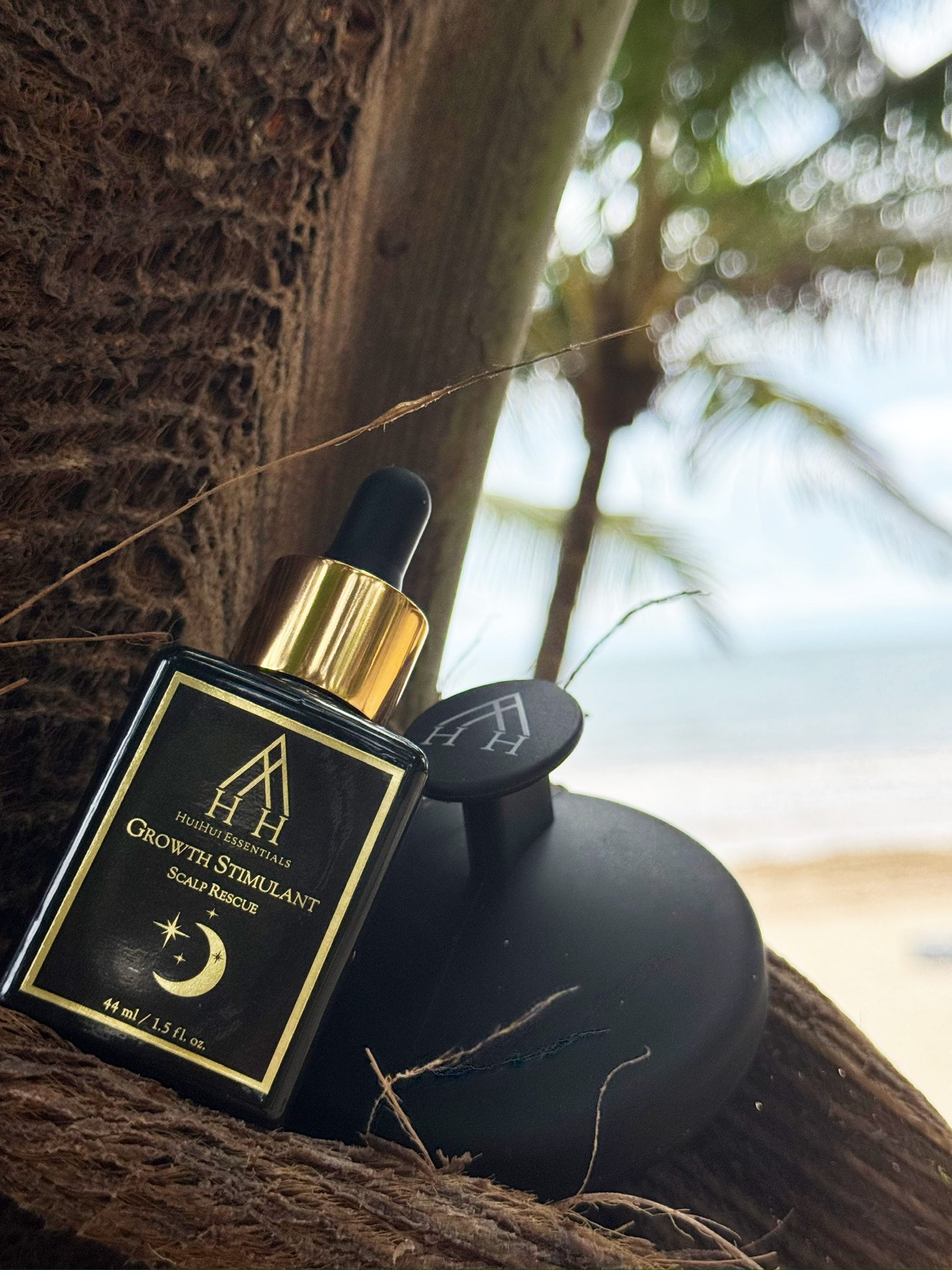A bottle of Huhiui Essentials Growth Stimulating Scalp Rescue serum lying on a tree branch, with a blurred background of sky and trees.