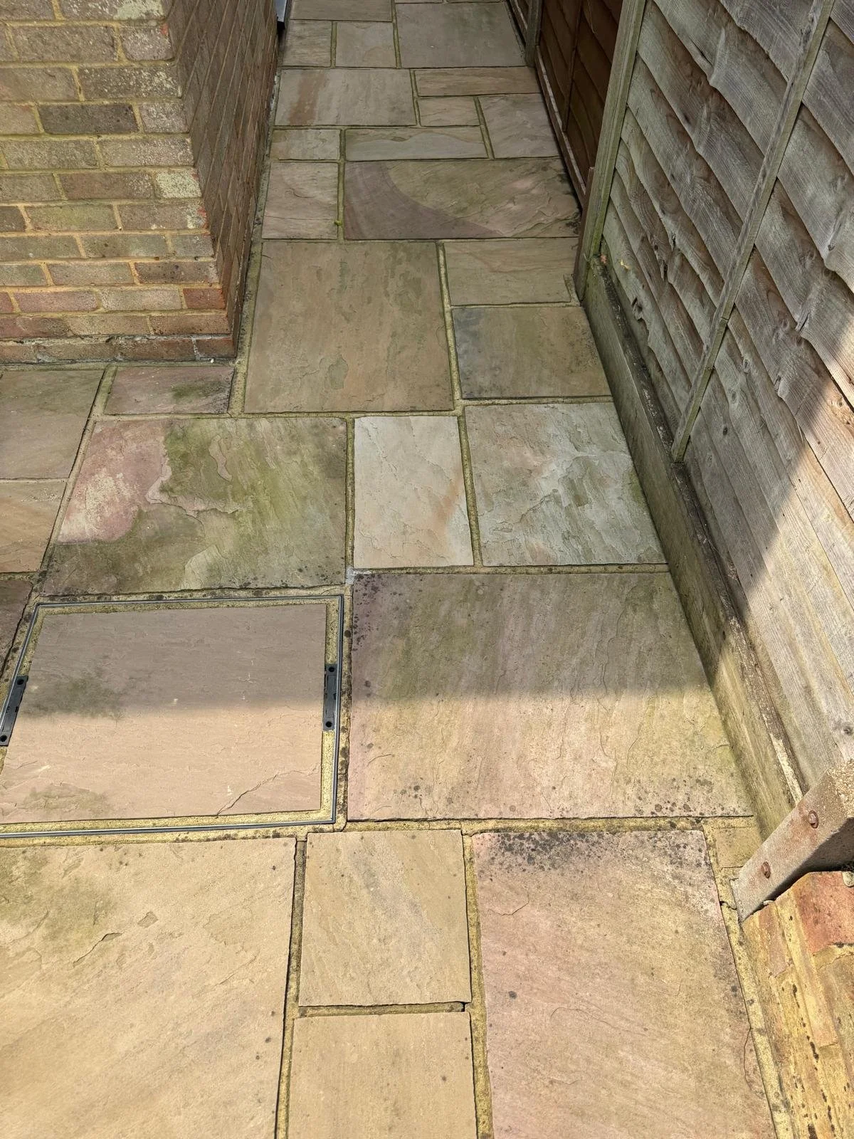 Heavily weathered sandstone garden path with algae and faded colour before cleaning.