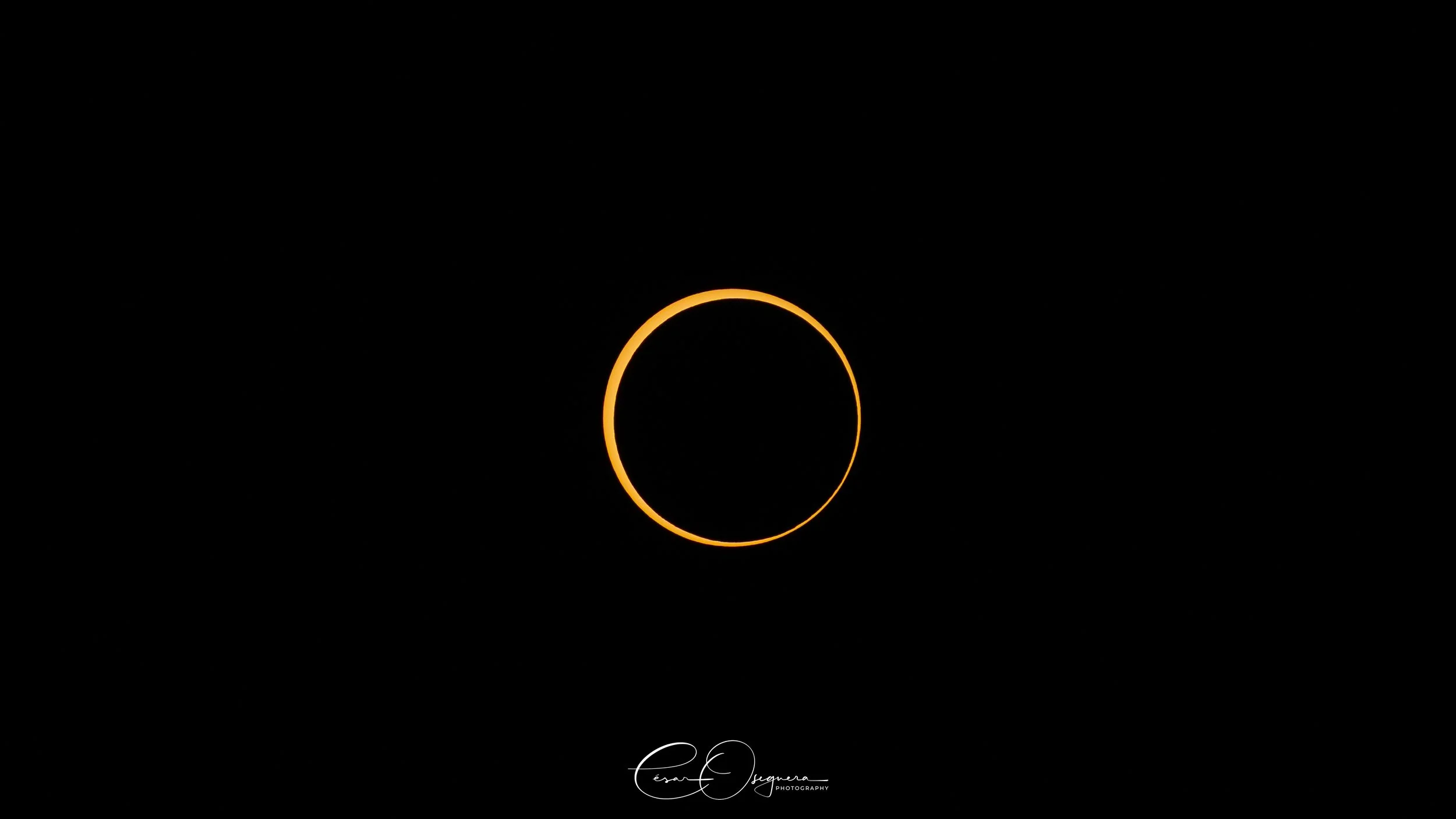 A solar eclipse showing the moon partially covering the sun, creating a dark circle with a bright ring around it against a black background.