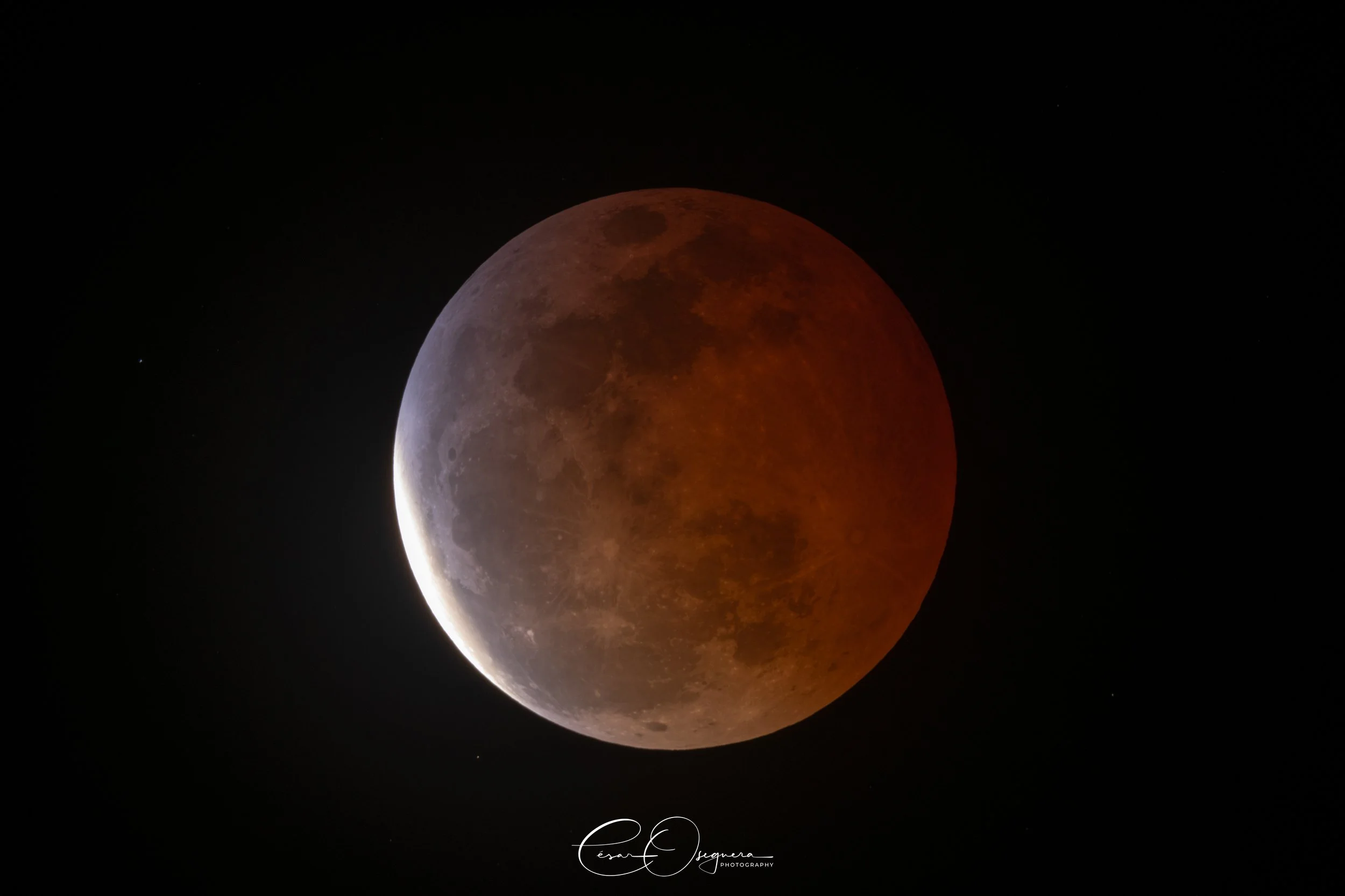 A photograph of a lunar eclipse showing the moon partly in shadow with a reddish hue on part of its surface against a dark night sky.