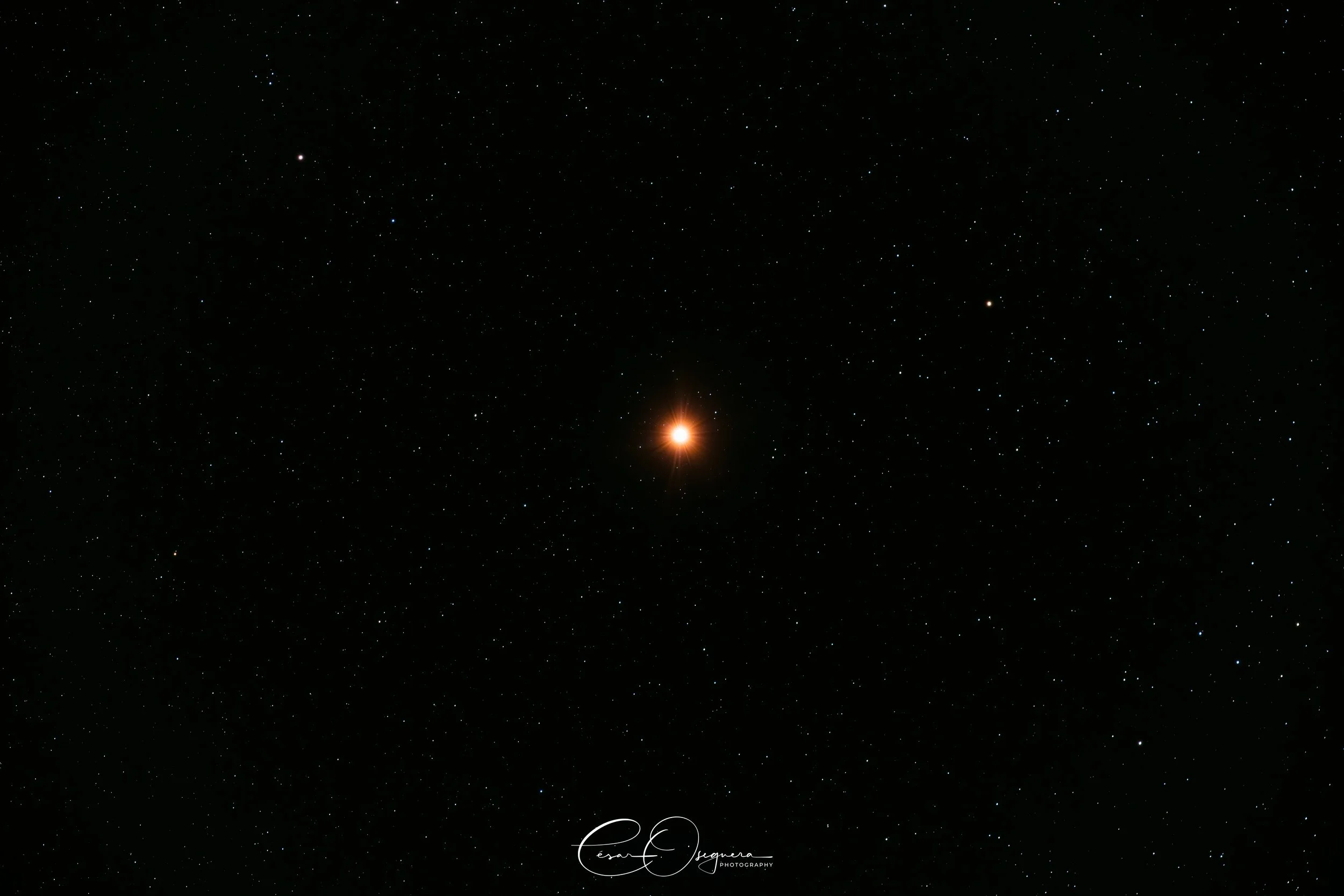 A starry night sky with a bright, glowing star at the center, surrounded by numerous smaller stars in a dark sky.