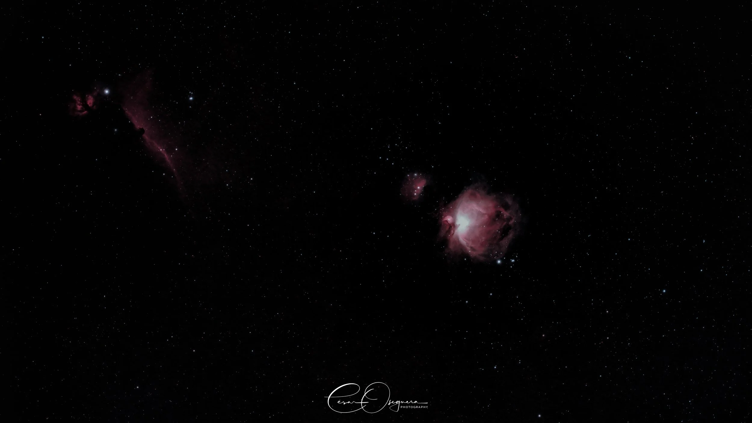 A wide view of space featuring the Orion Nebula, a bright, colorful nebula with pink and white hues, surrounded by numerous stars against the blackness of space.