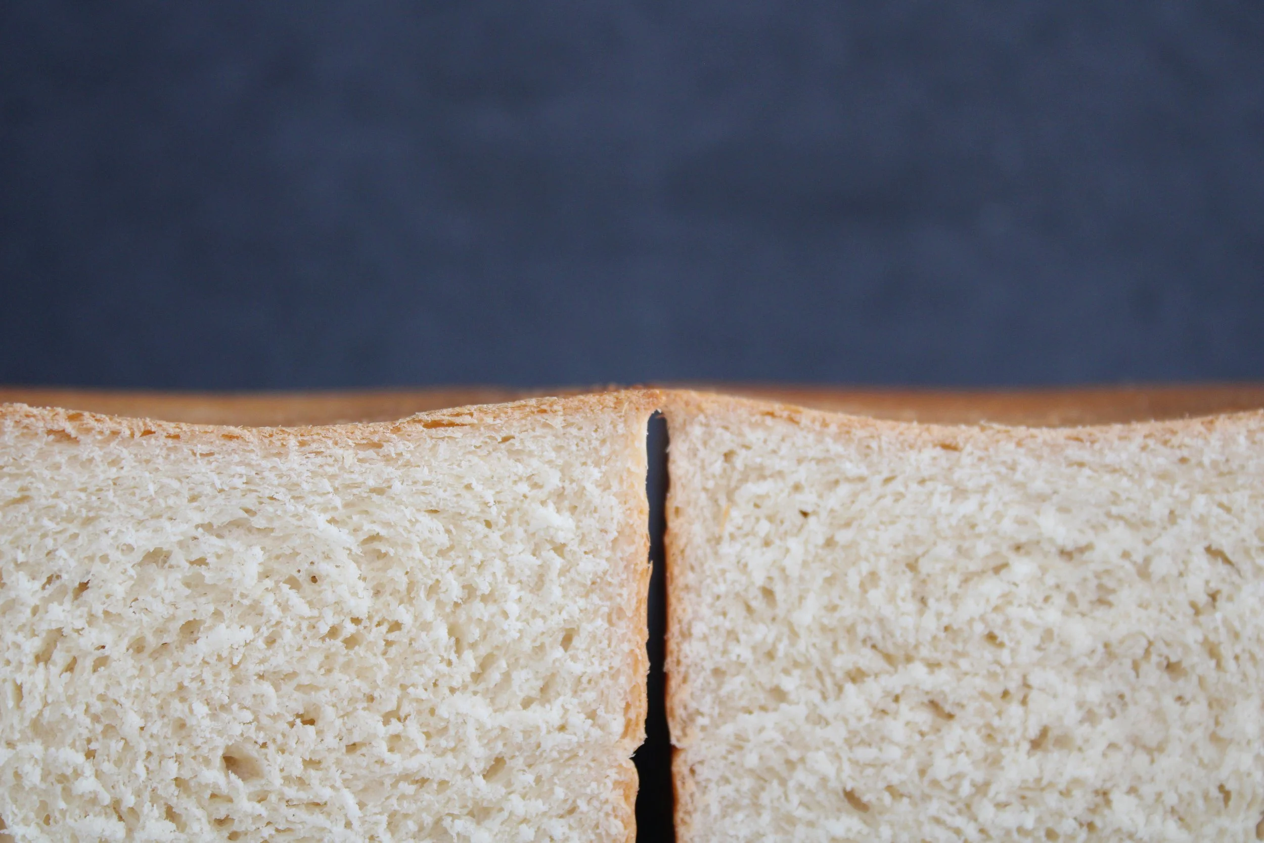 Close-up of a sliced loaf of bread showing the soft, airy interior against a dark background.