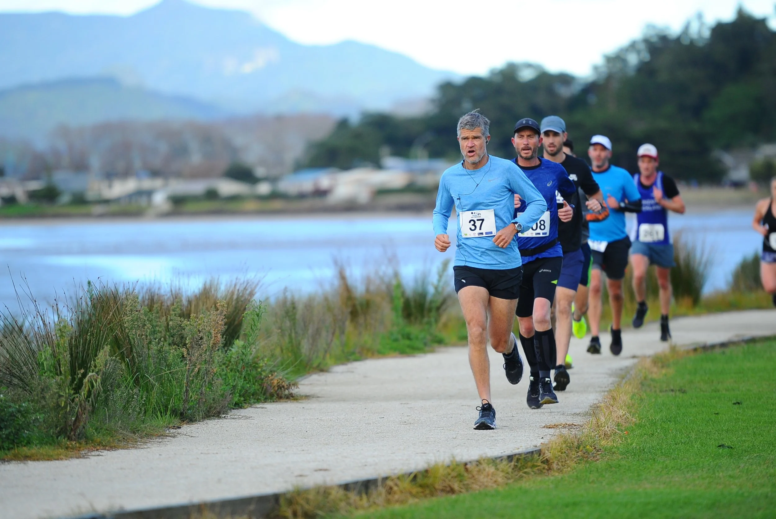 Group of people running in a race on a lakeside path.