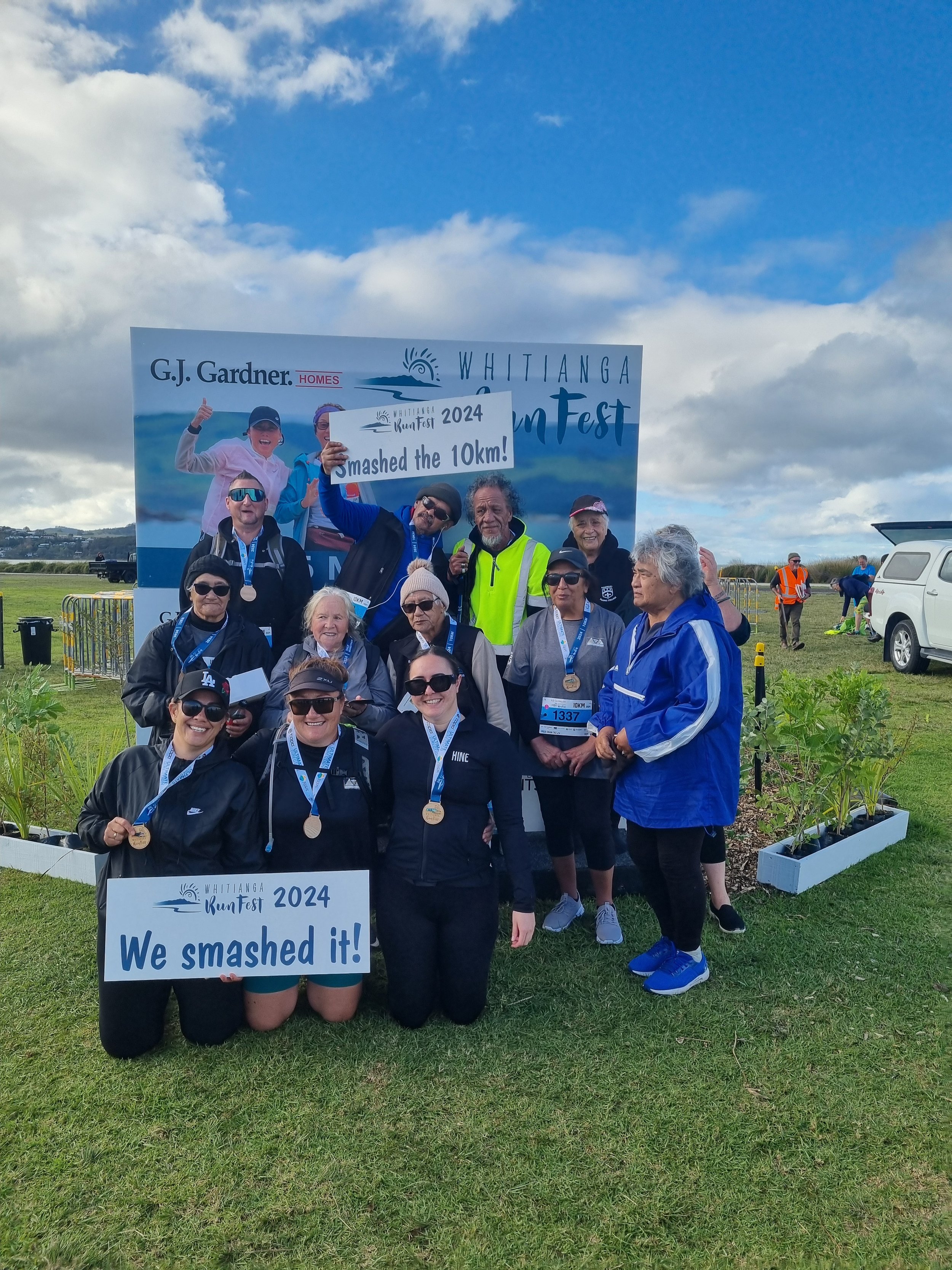 Group of people celebrating after completing a 10km run at Whitianga RunFest 2024, holding signs and medals.