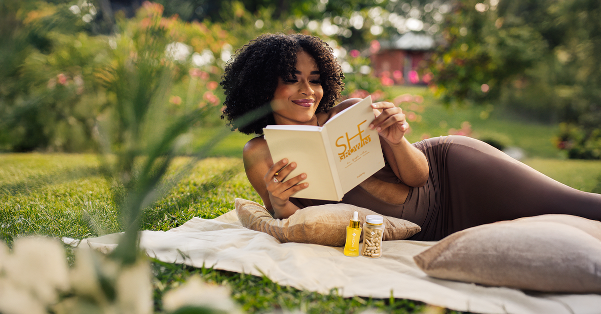 A black woman reading a journal on top of a blanket at the park