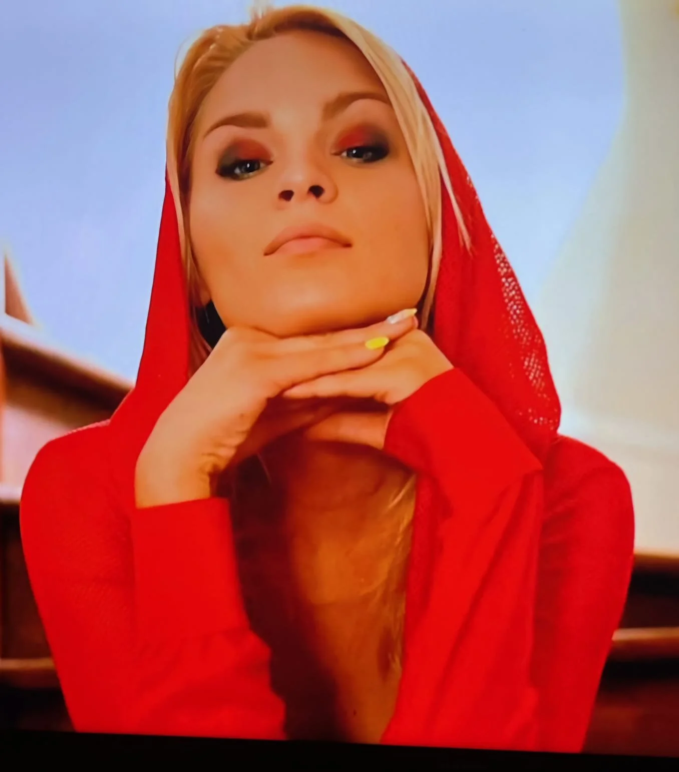 Person in red top and hood resting chin on hands, looking forward.