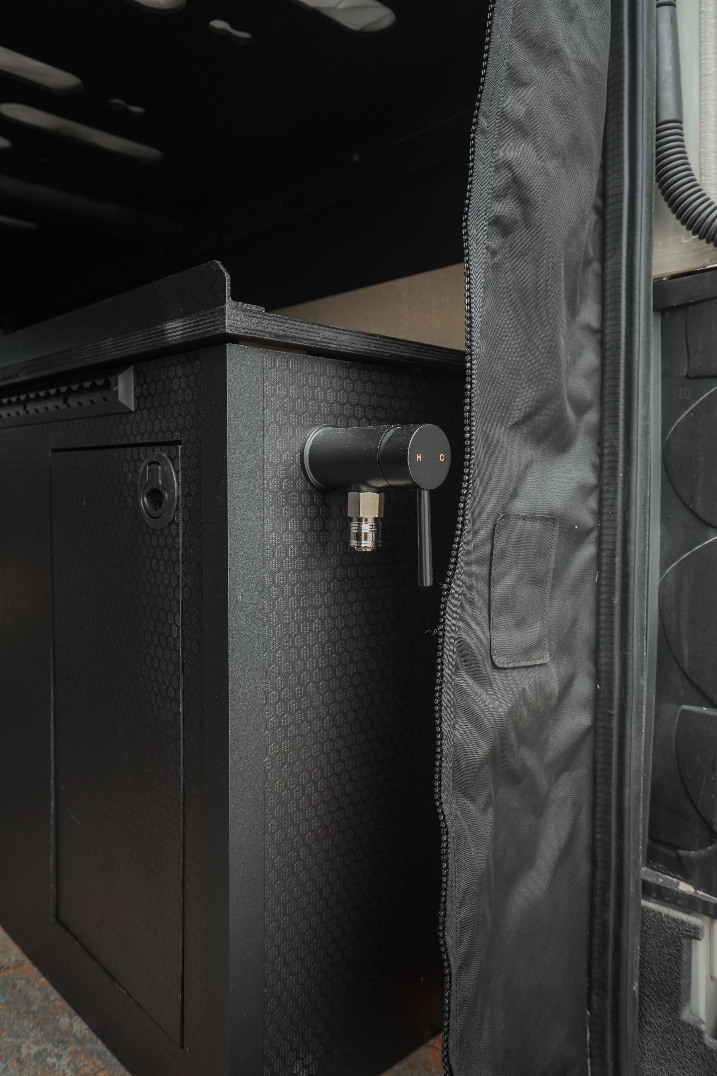 Close-up of a portable black speaker with a textured surface, placed on a dark surface next to a black fabric case with a zipper.