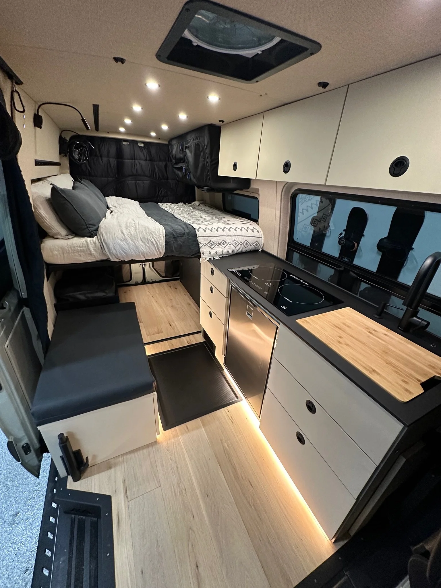 Interior of a modern camper van with a bed, kitchen, and storage compartments.