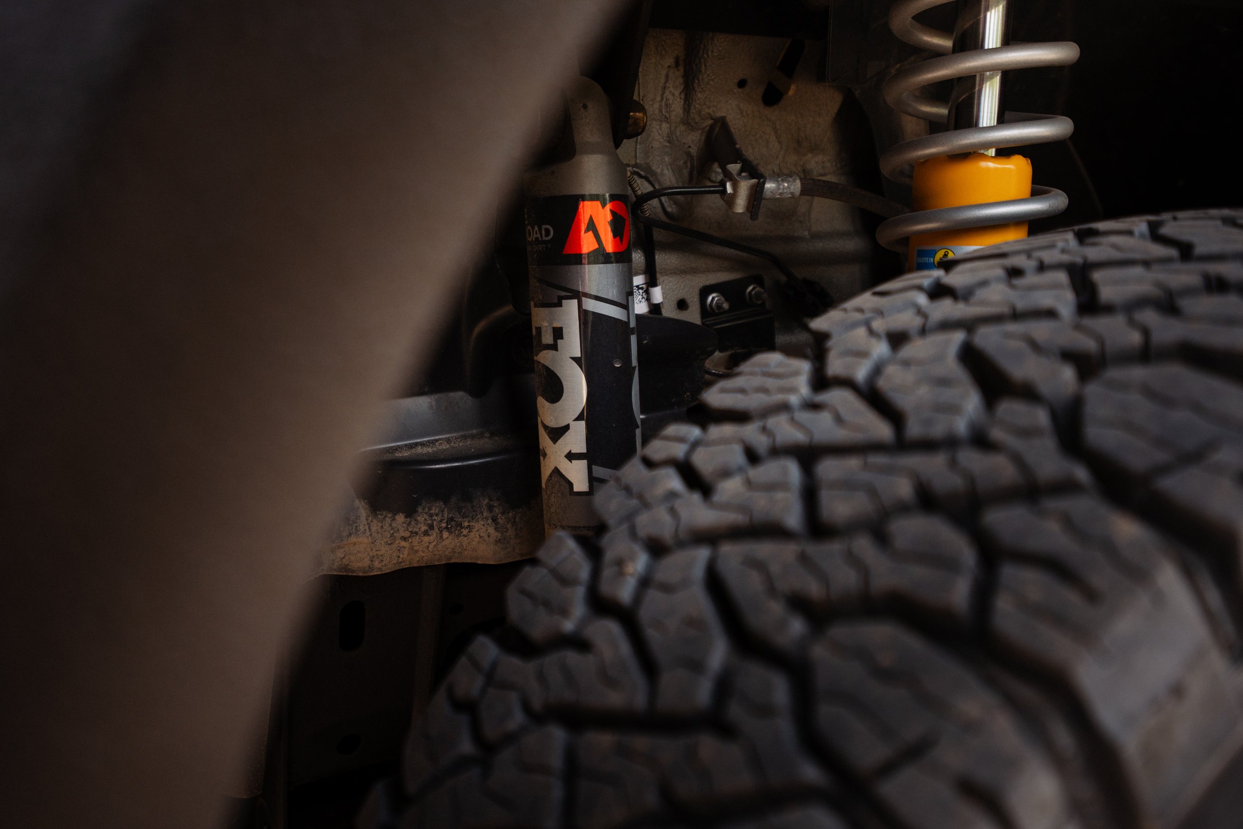 Close-up of an off-road vehicle suspension system showing a shock absorber with a yellow coil spring and a tire with an aggressive tread pattern.