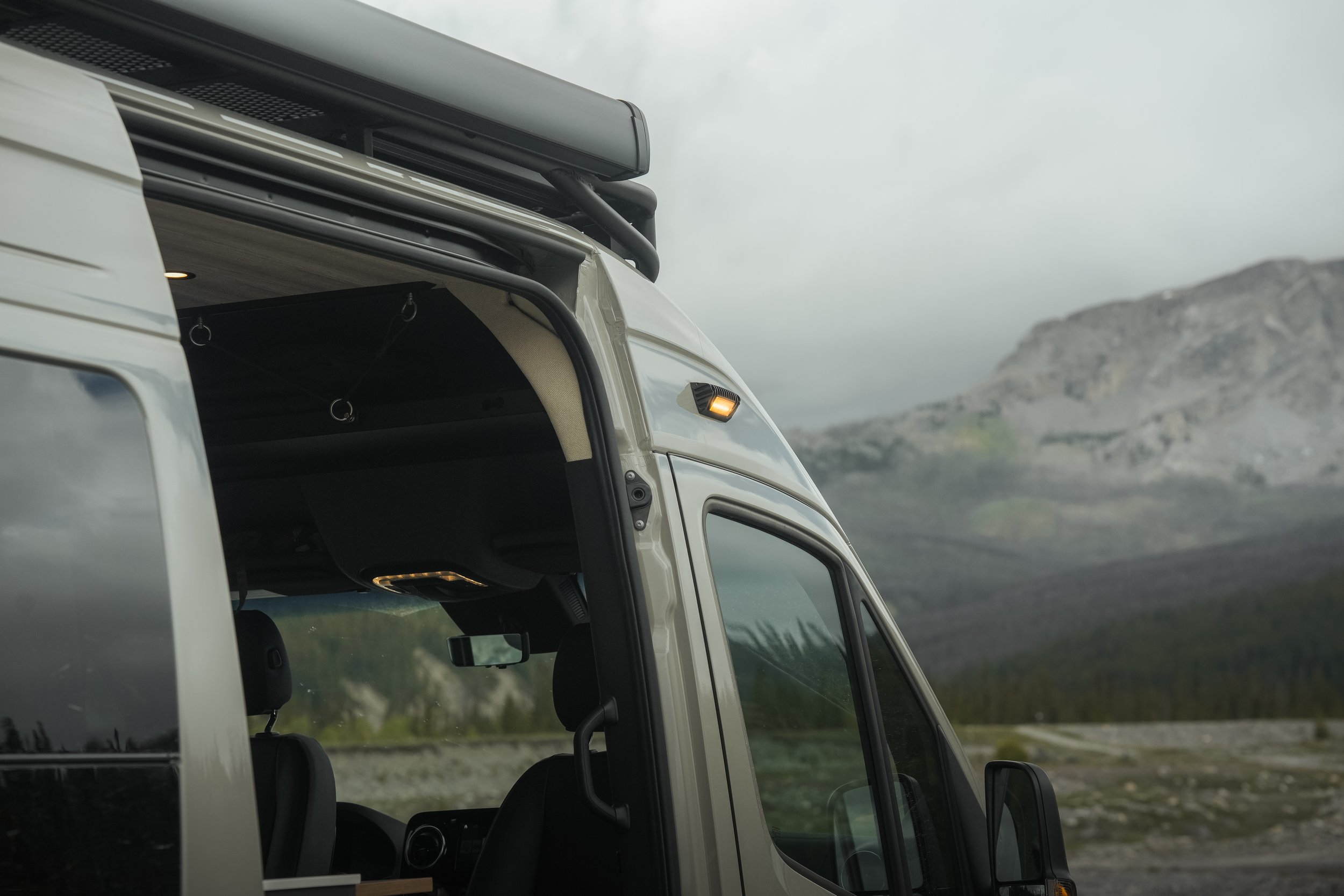 Close-up of the front part of a white vehicle, showing part of the interior and exterior, with a nature landscape and cloudy sky in the background.