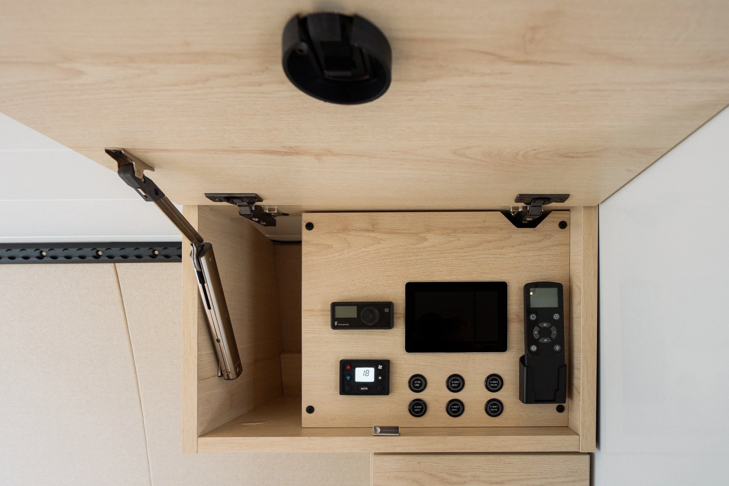 A wooden control panel with various electronic devices and switches mounted inside a cabinet, including a digital thermostat, remote control, and other control units.